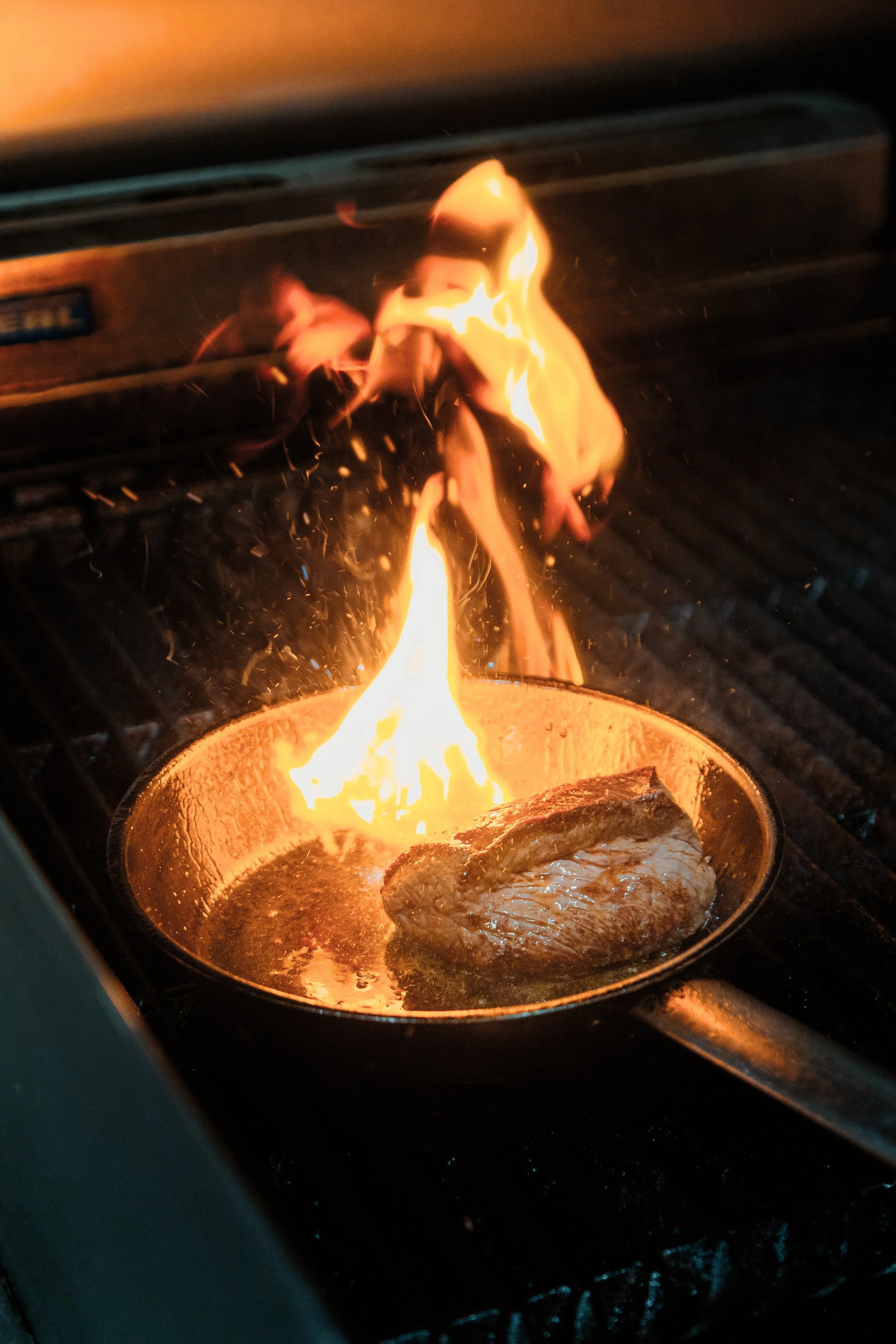 A piece of meat cooking in a frying pan over an open flame on a stove. york leeds yorkshire restaurant photographer videographer. corner grill house york