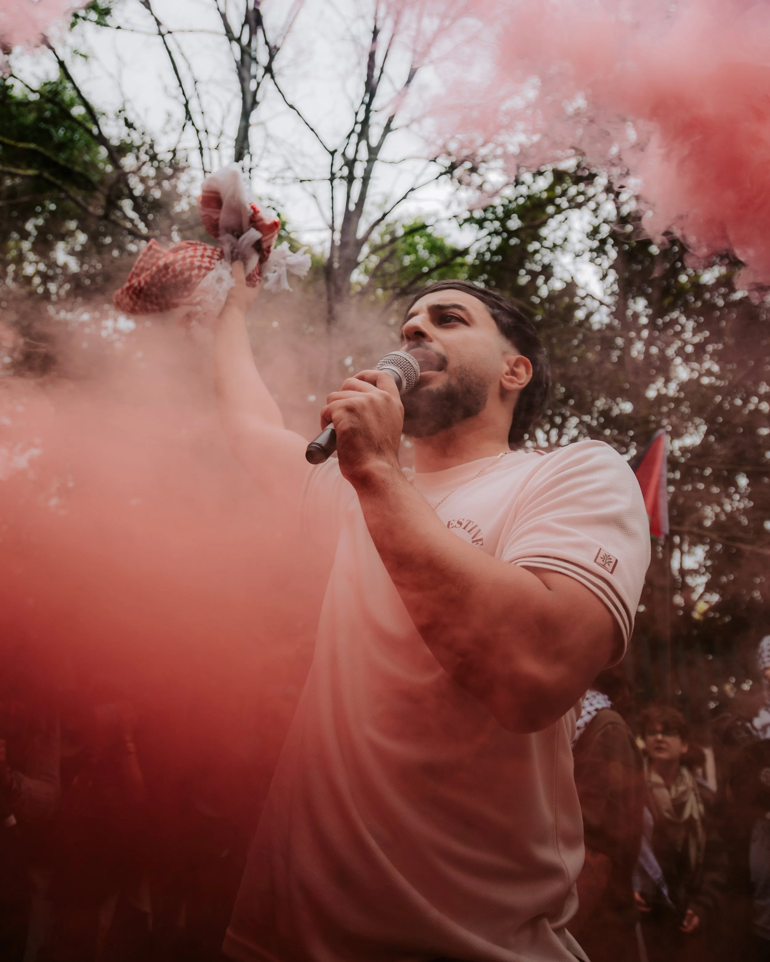 Man chants at pro palestine protest with red flare holding a keffiyeh