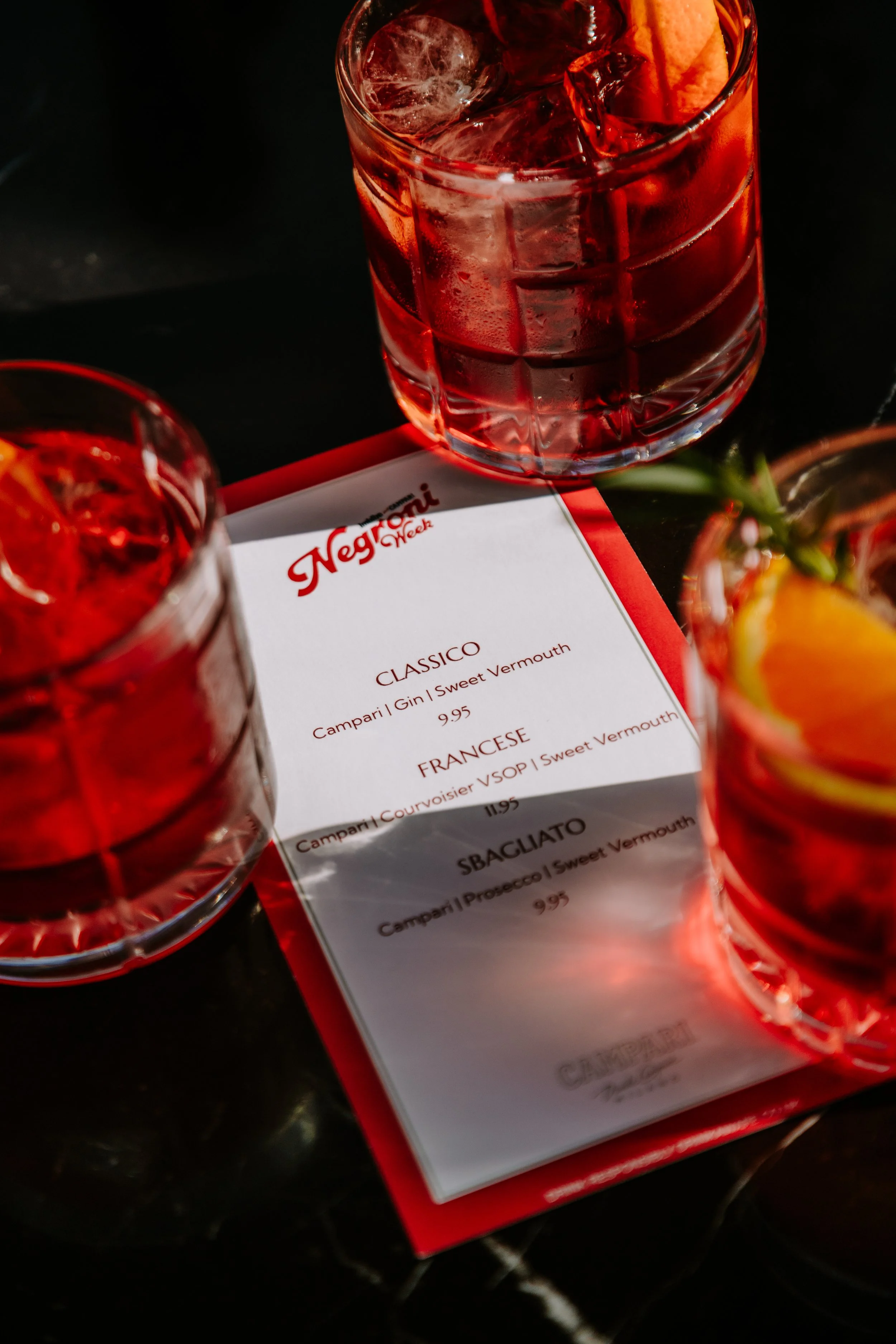 Close-up of a glass of red cocktail with ice, placed on a table next to a food menu with red and white colors, partially visible. york leeds yorkshire restaurant photographer videographer