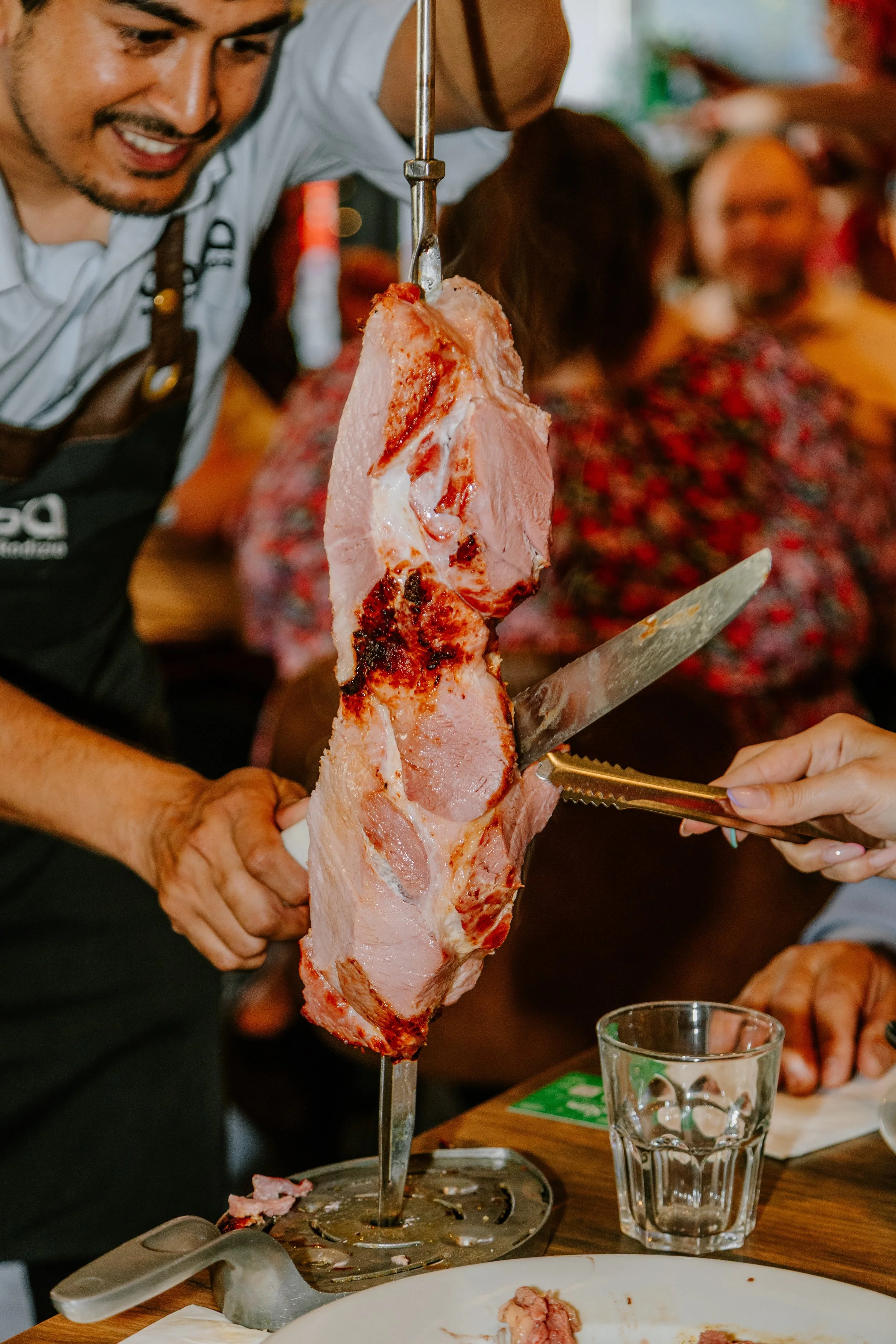 Person carving a large piece of cooked meat, likely ham, at a restaurant. york leeds yorkshire restaurant photographer videographer. casa brazilian rodizio york.