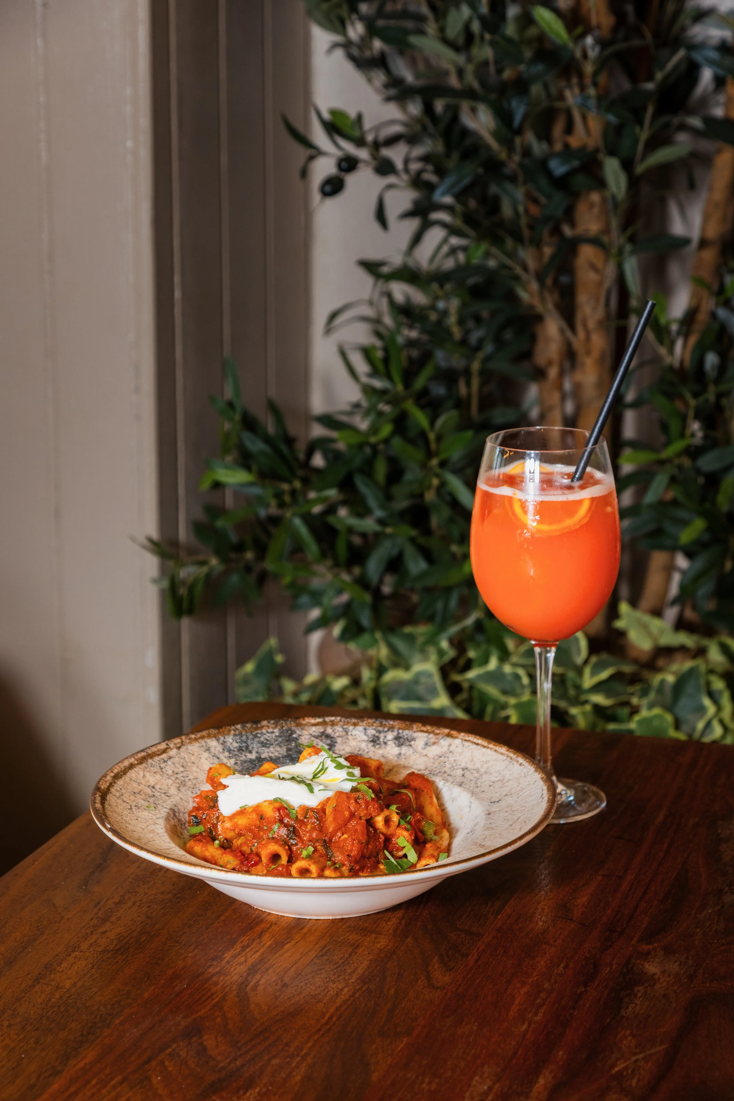 A bowl of pasta with tomato sauce, garnished with fresh herbs and a dollop of sour cream, placed on a wooden table. york leeds yorkshire restaurant photographer videographer
