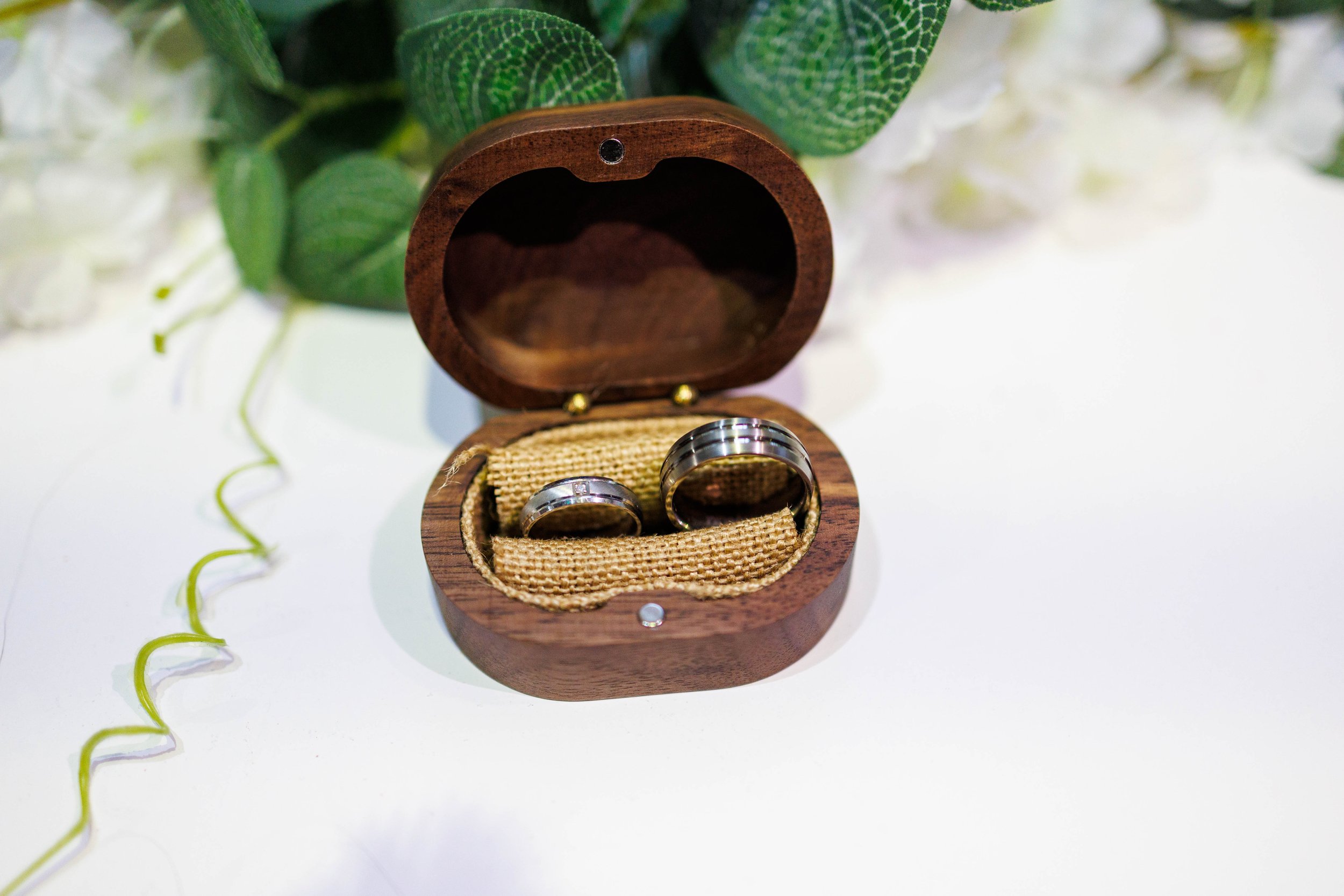 Two silver rings in a wooden box with green leaves in the background.