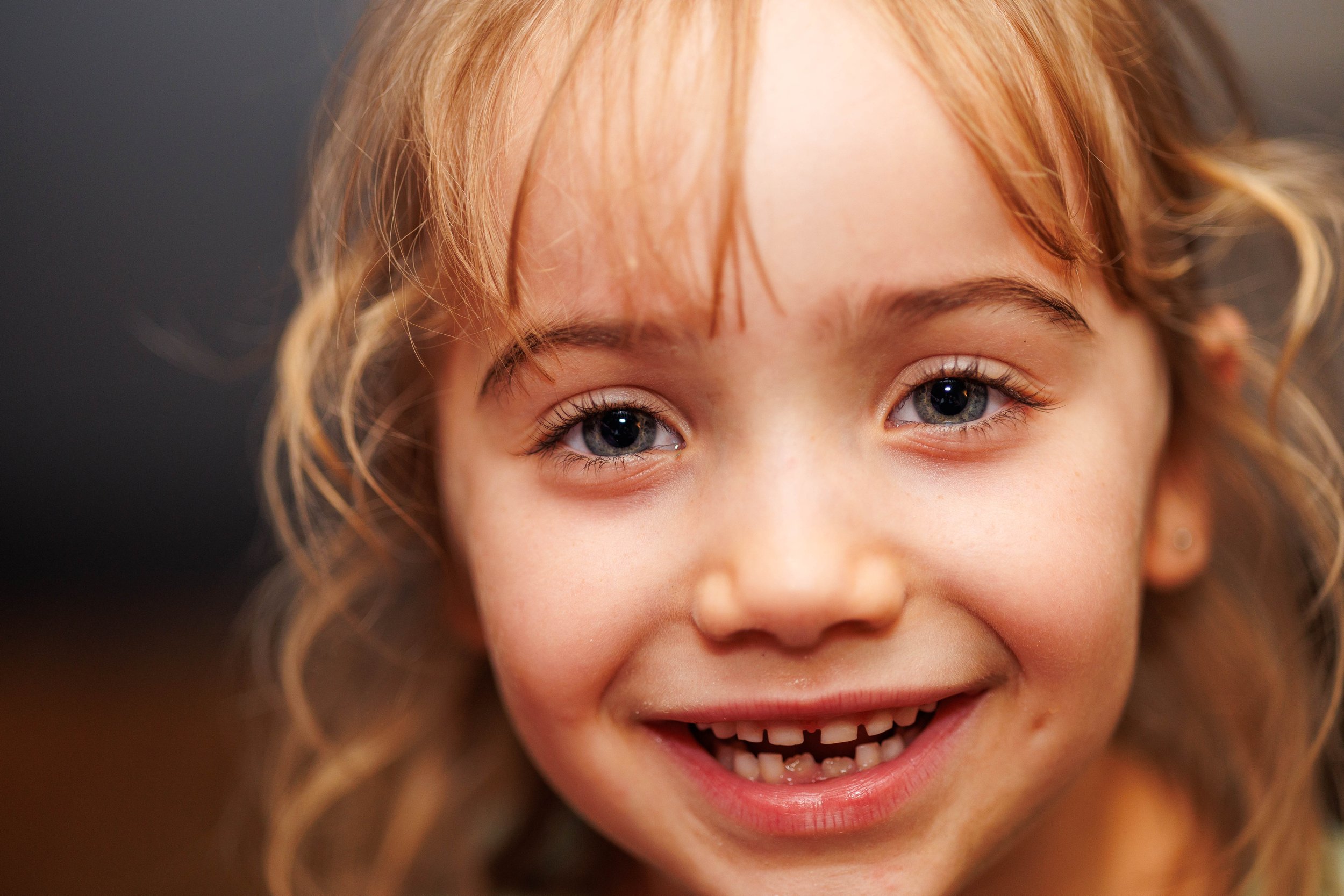A close-up of a smiling child with blond hair and blue eyes.