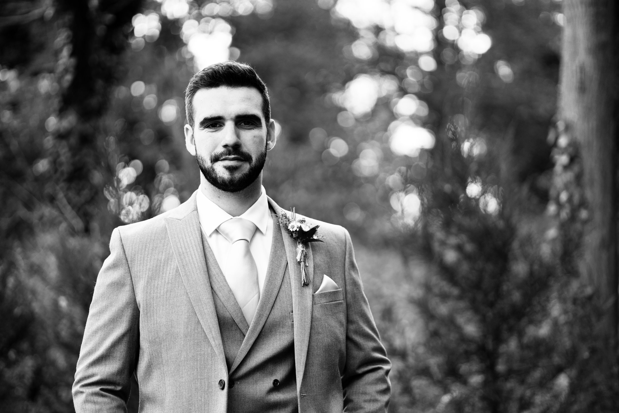 A groom wearing a suit with boutonniere outdoors, black and white photo