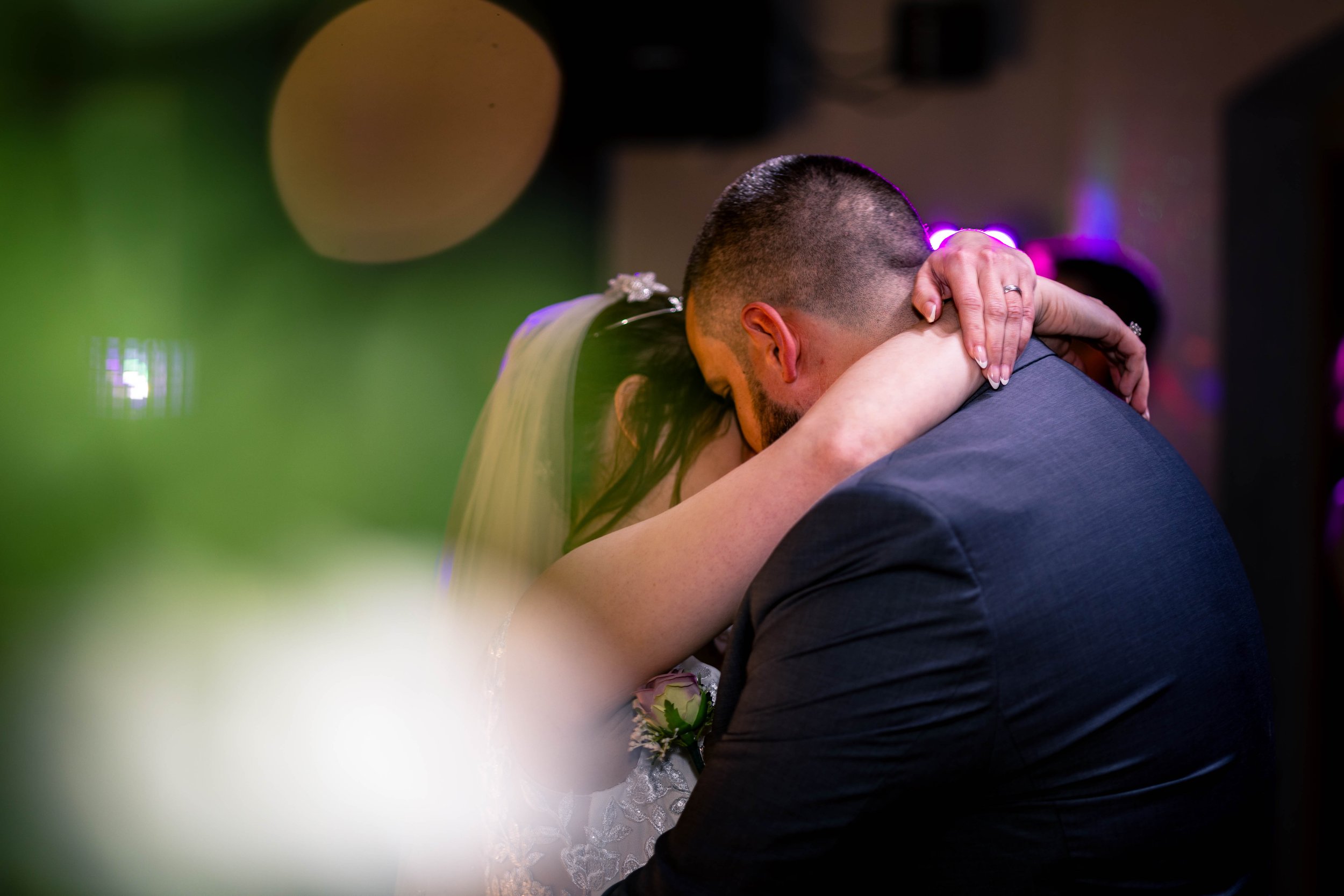 Wedding couple kissing with vibrant lighting and blurred greenery in foreground.