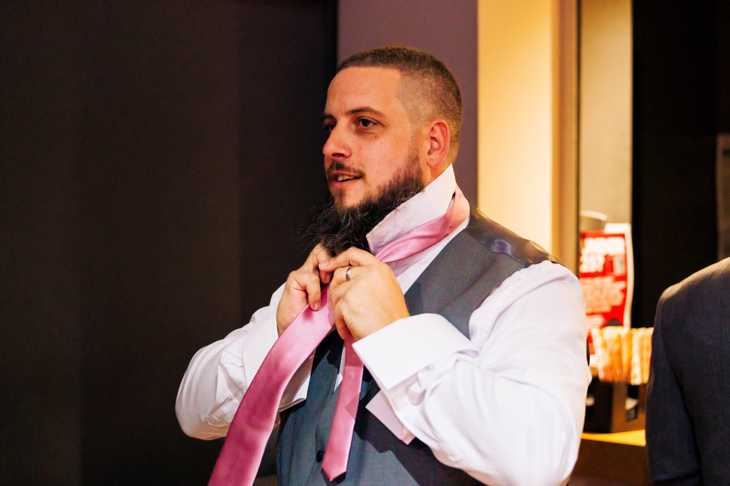 Man in a gray vest, white shirt, and pink tie preparing for an event.