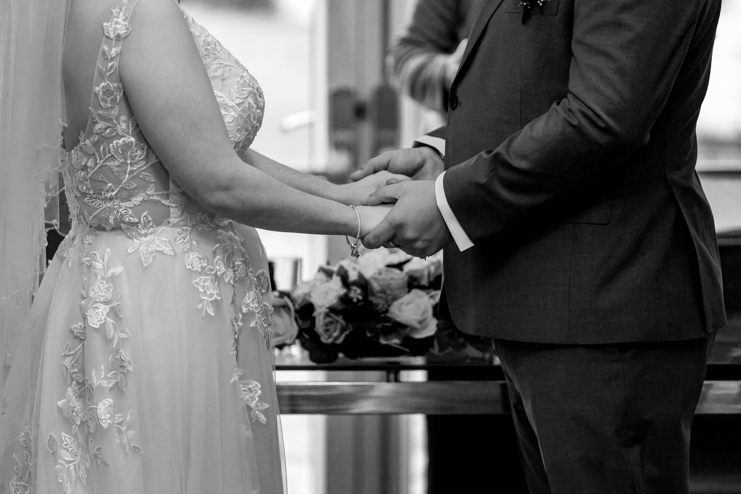 Bride and groom holding hands during a wedding ceremony, captured in black and white.