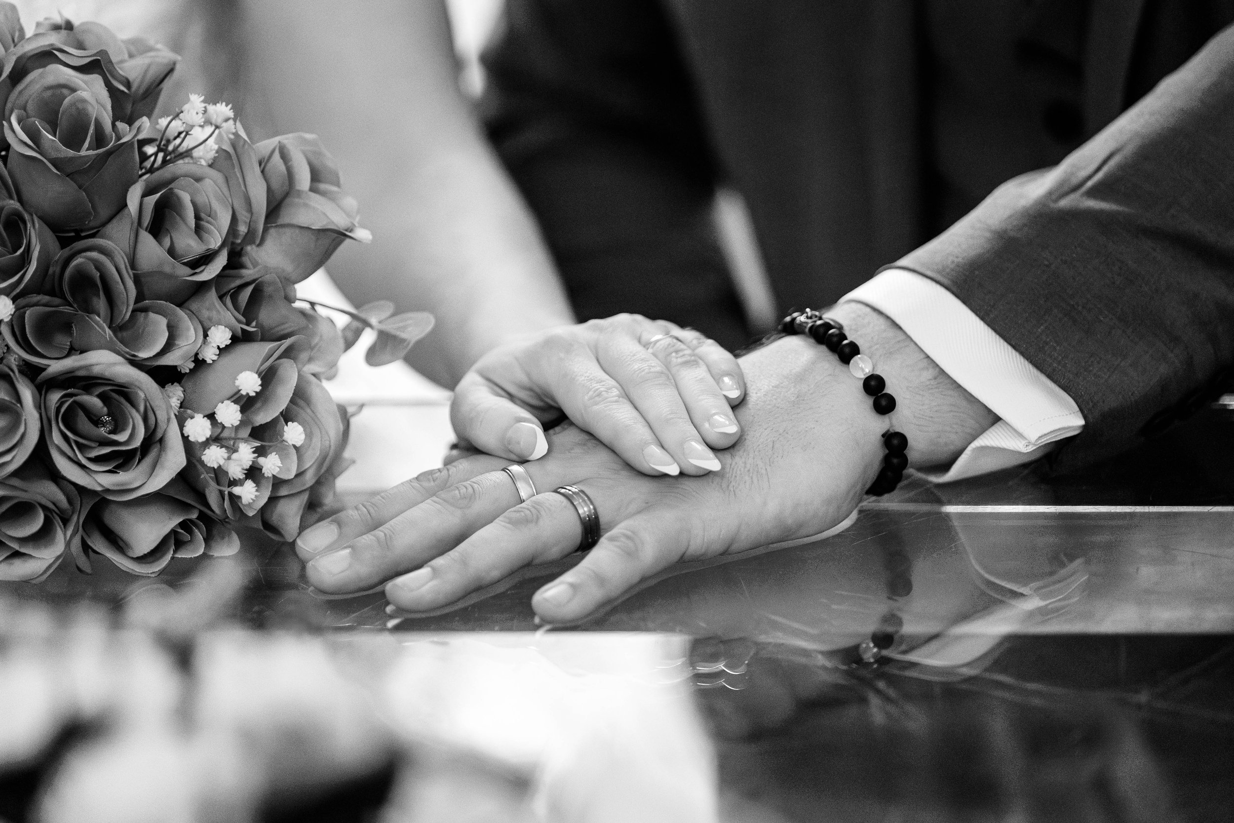 Close-up of a couple's hands with wedding rings and a bouquet in black and white.