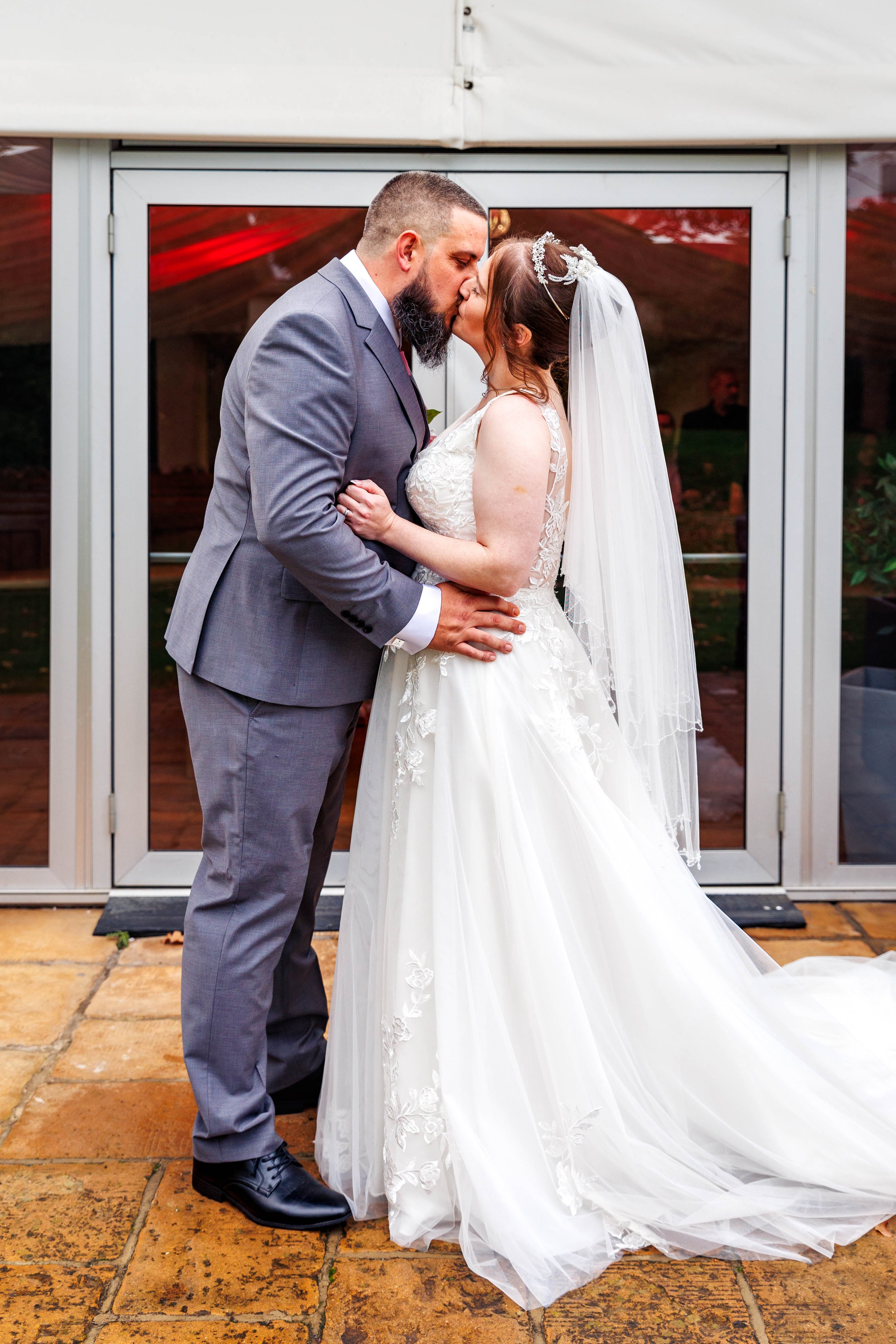 Bride and groom kissing in front of a glass door at a wedding ceremony.