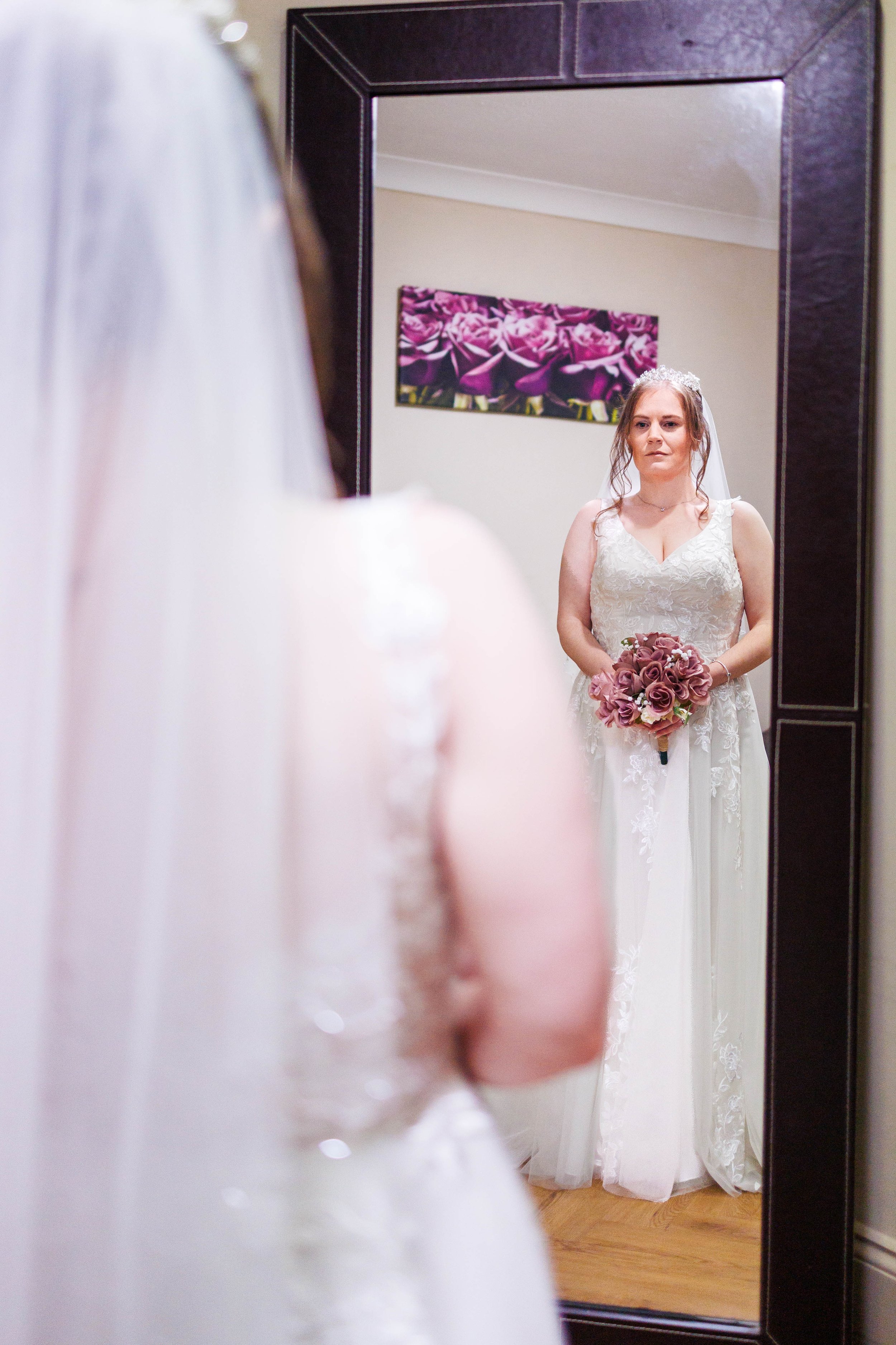 Bride in a wedding dress holding a bouquet, reflected in a mirror.