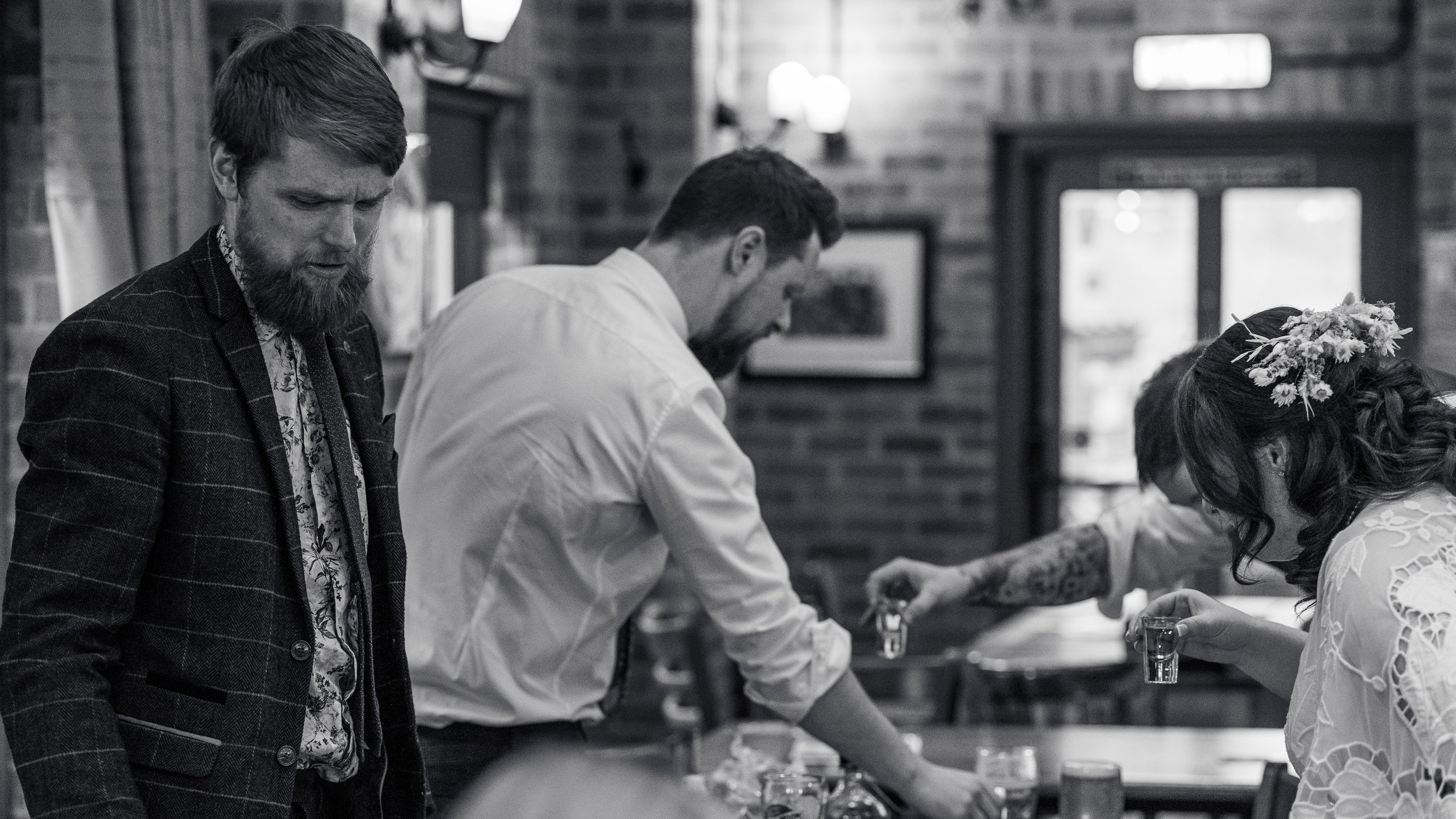 People in a bar setting, pouring shots and talking, black and white photo.