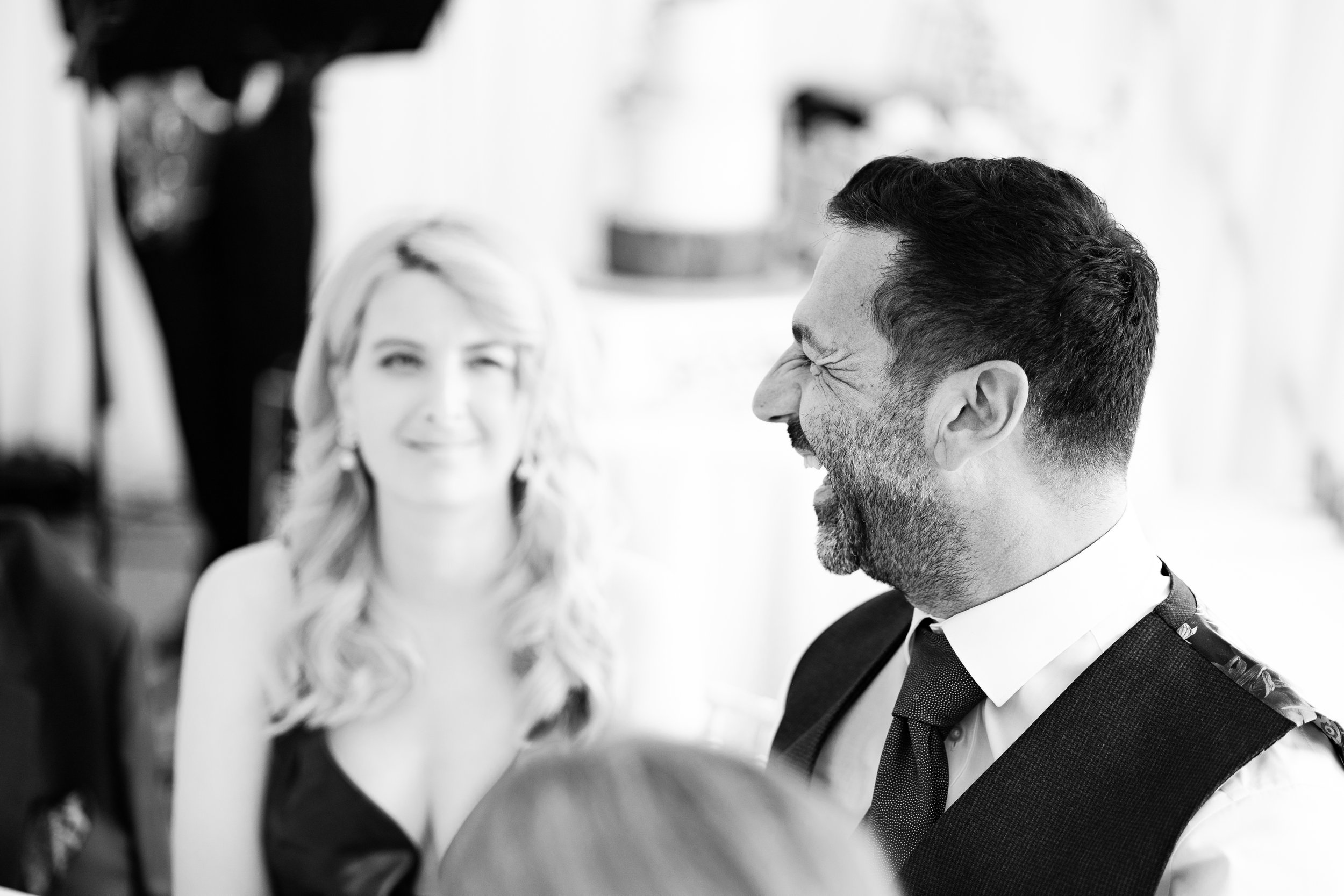 Black and white photo of a man laughing and a woman smiling at a formal event.