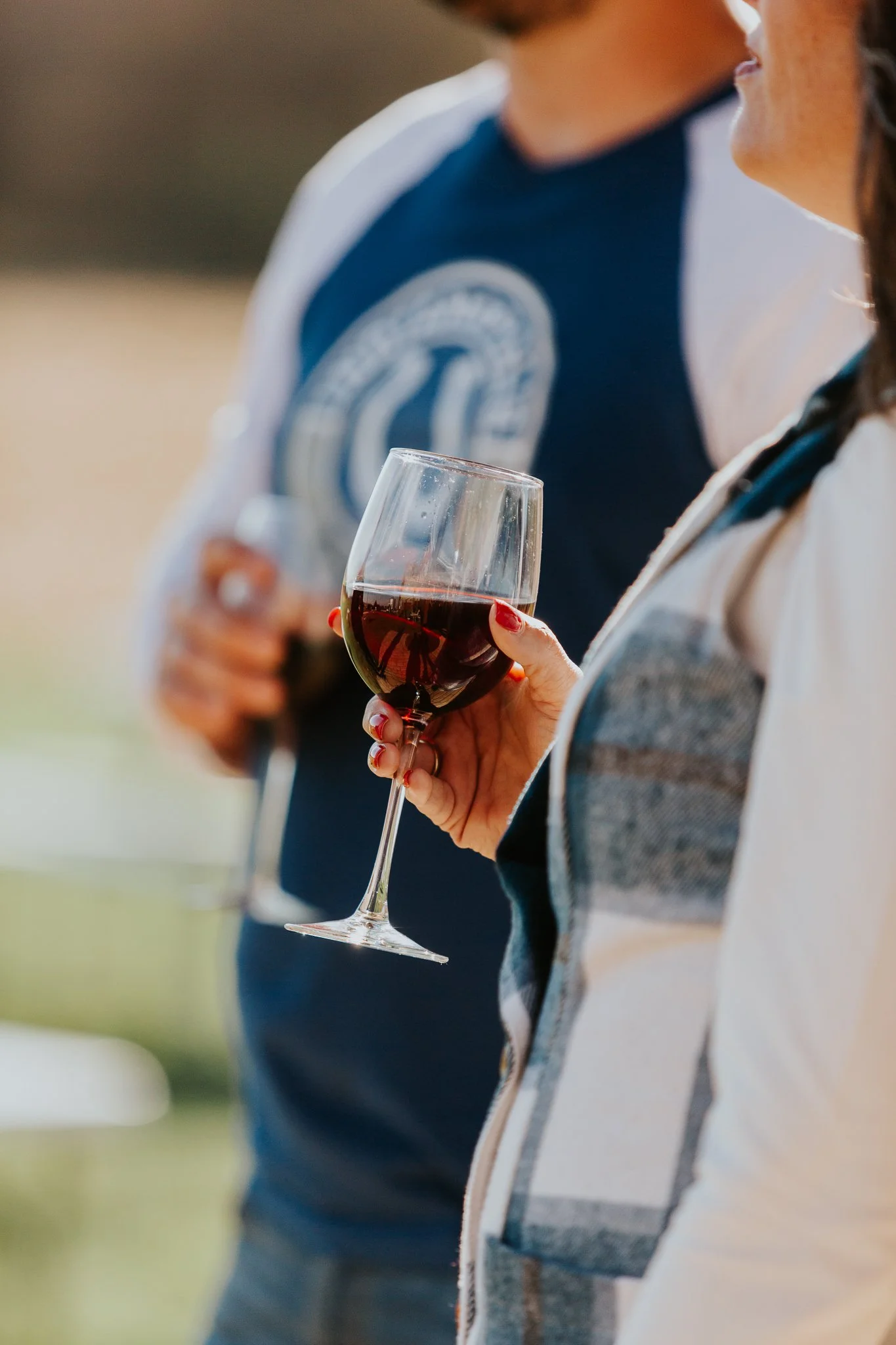 A close-up of women holding wine glasses filled with red wine during an outdoor gathering or event.