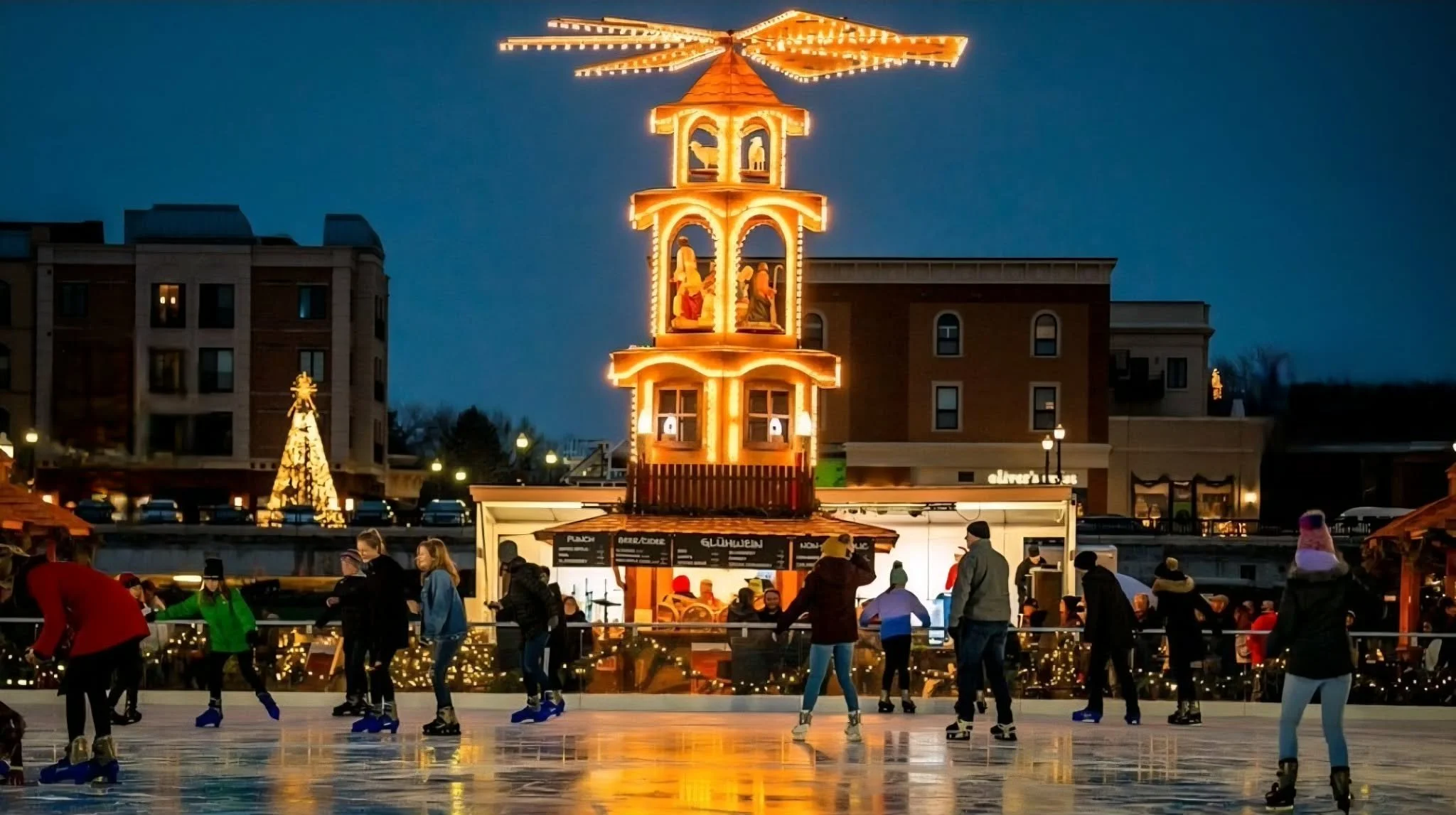 People ice skating at an outdoor rink during the evening, with a lit-up Christmas tower and decorated Christmas tree in the background. Carmel Christkindlmarkt