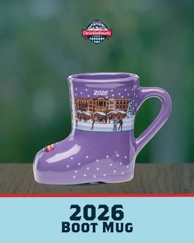 A purple boot-shaped mug with Christmas 2026 scene and snow, displayed on a wooden surface against a green background. Carmel Christkindlmarkt