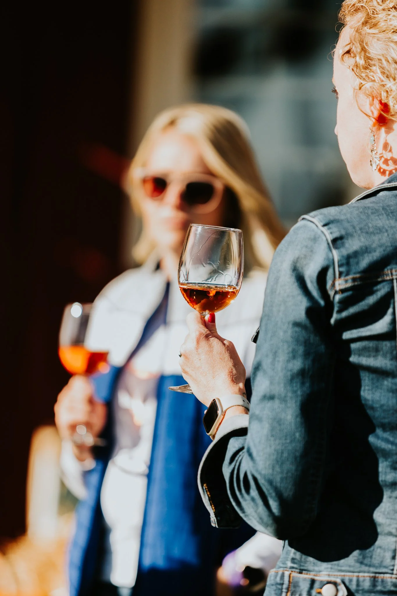 Close-up of women holding glasses of rosé wine at an outdoor gathering on a sunny day. Rose all day! Friends drinking wine. Outdoor seating area to enjoy wine with friends.