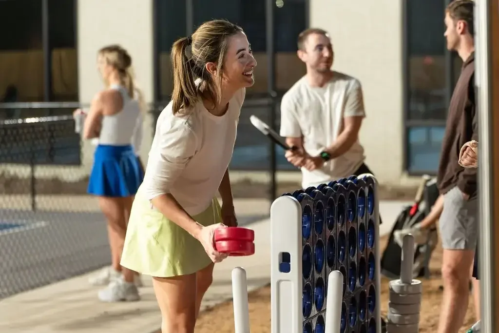 A woman playing giant Connect Four with a man at an outdoor social gathering during evening, with two other people in the background.