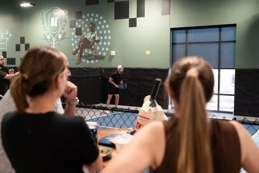 People watching a padel match through the glass at an indoor sports facility.
