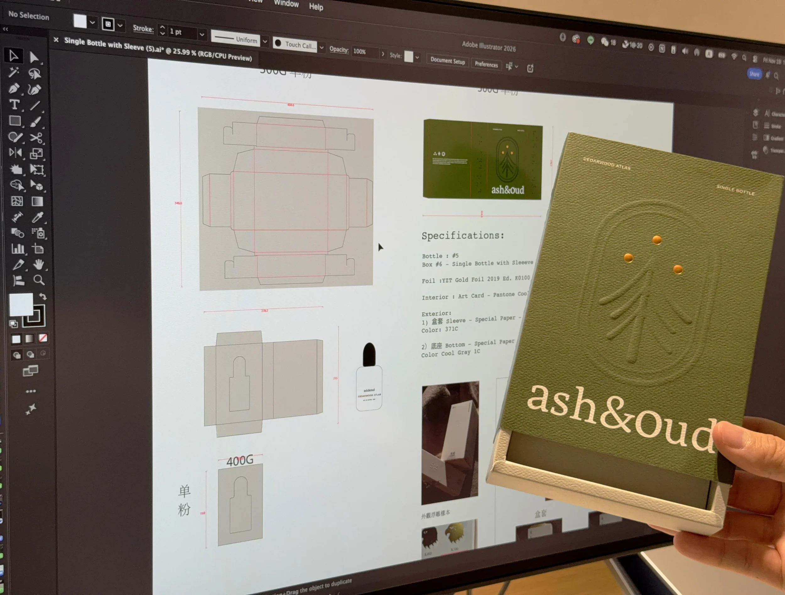 Person holding a green box of ash&oud single bottle packaging in front of a computer screen displaying packaging design drawings and specifications.