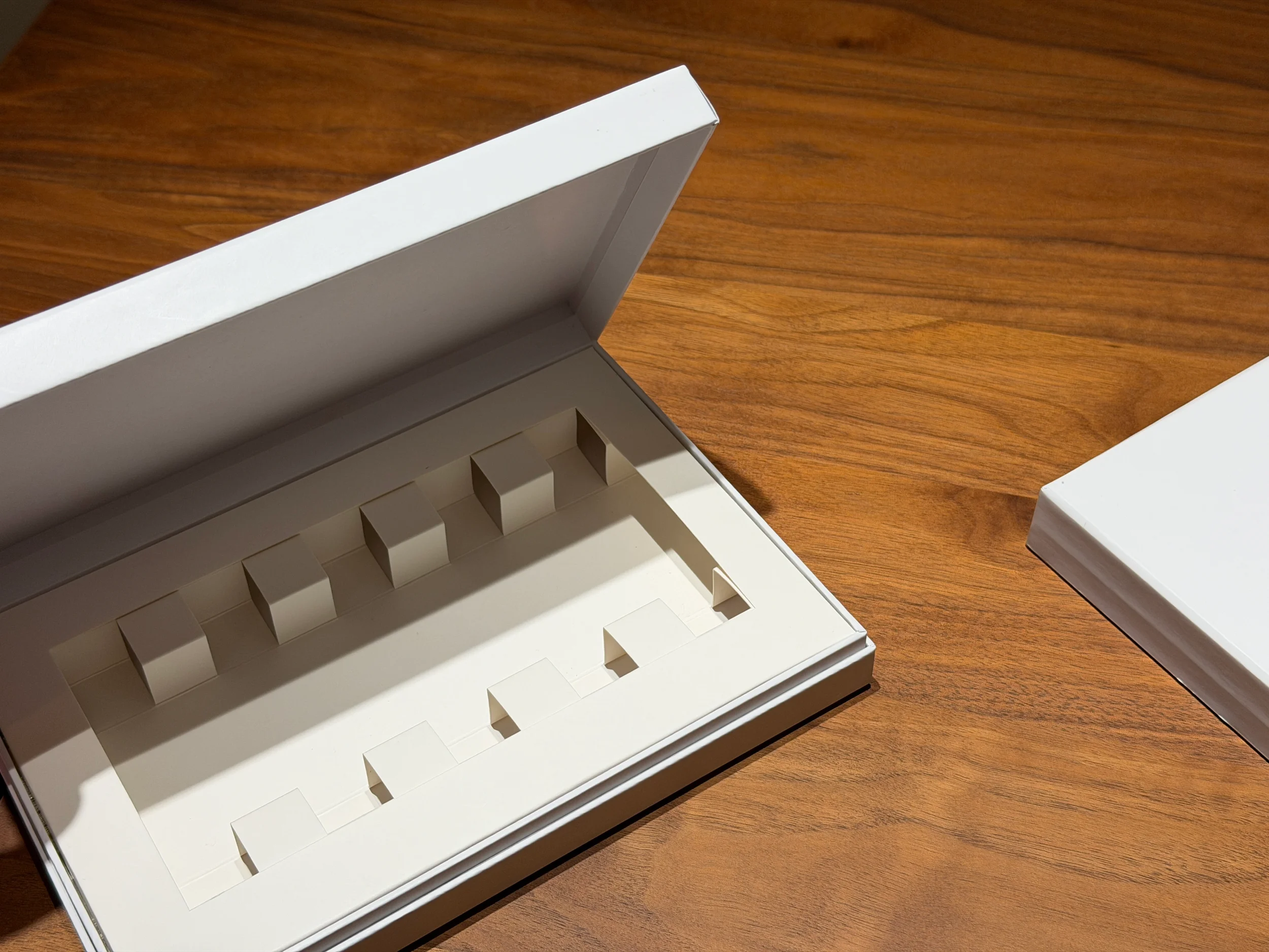 Open white box with compartments on a wooden surface, empty inside.