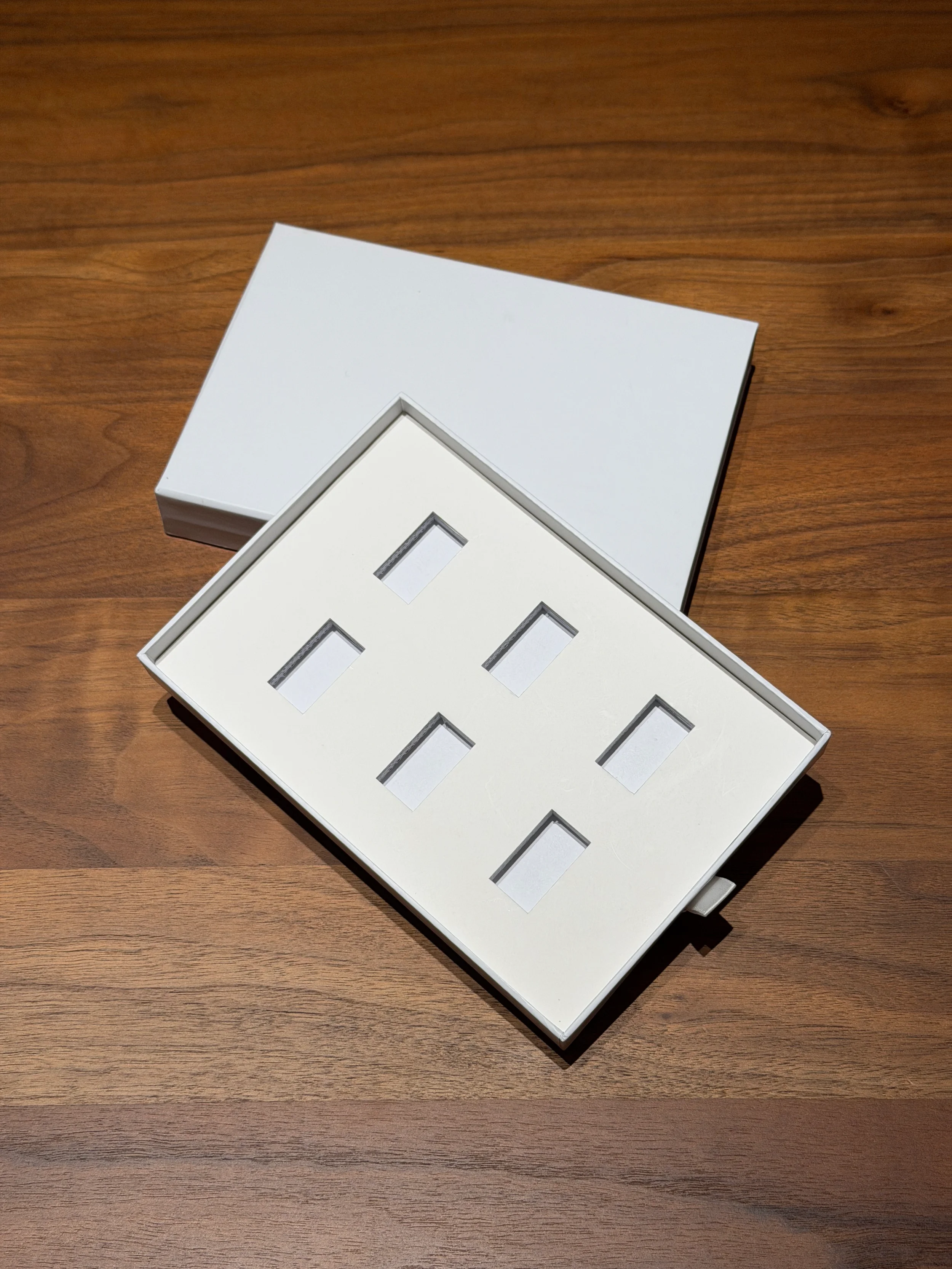 Open white box with empty slots for electrical outlets resting on a wooden table.