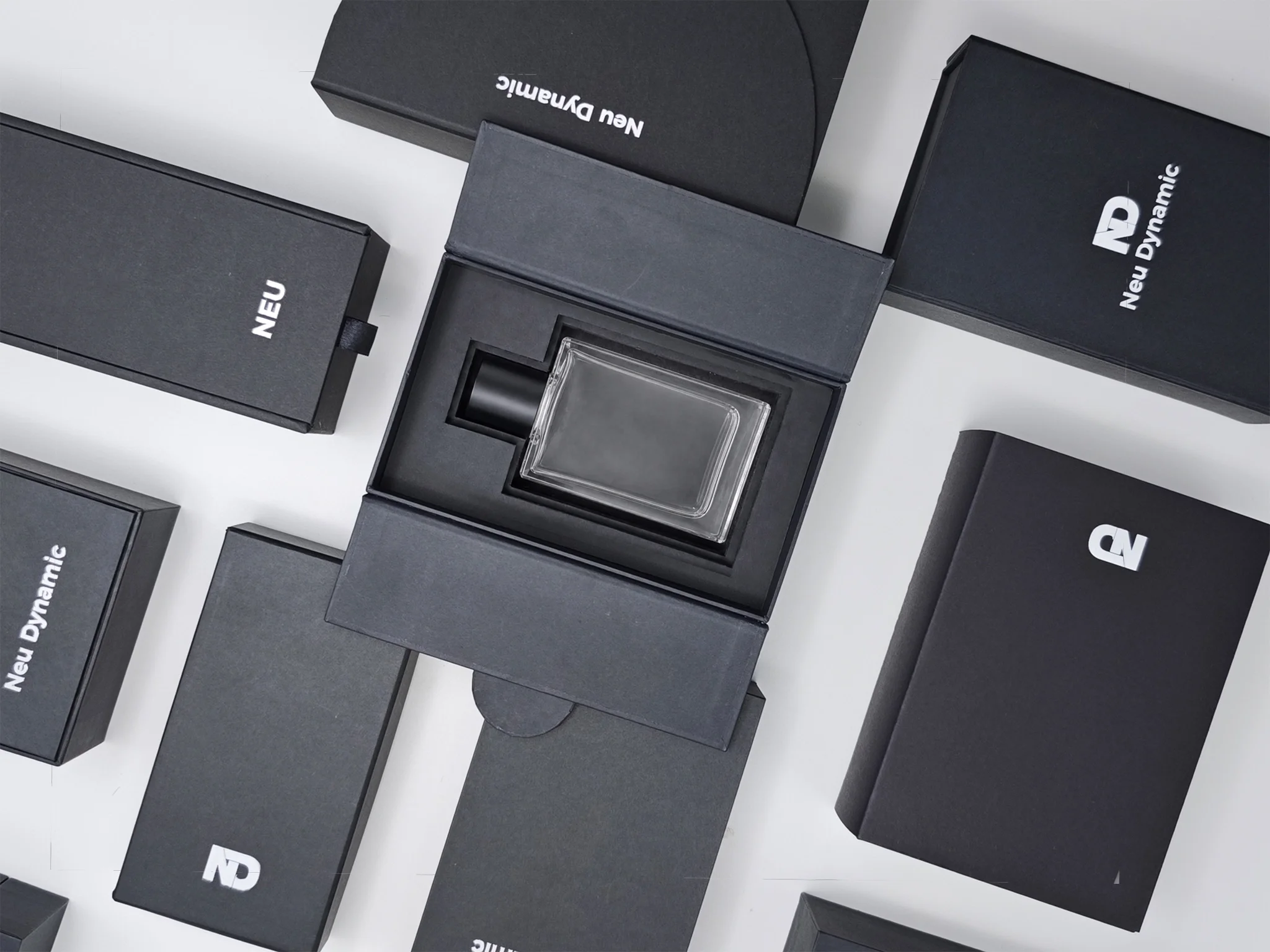 Close-up of black boxes with white text, reading "Neu Dynamic" and "ND Dynamic," stacked and arranged on a white surface, with one transparent object inside an open box.