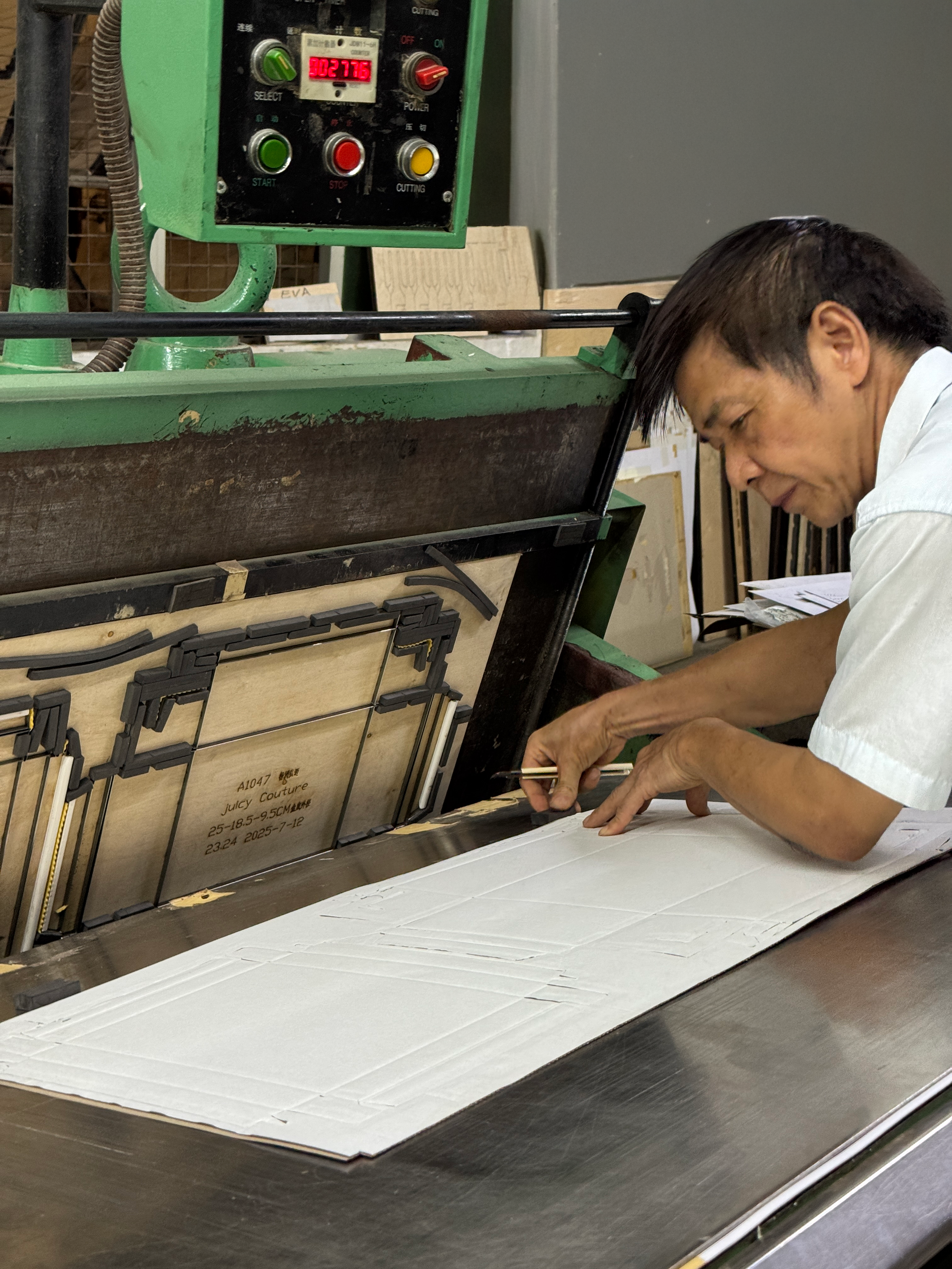 A man working on a craft project at a worktable with a green industrial machine in the background.