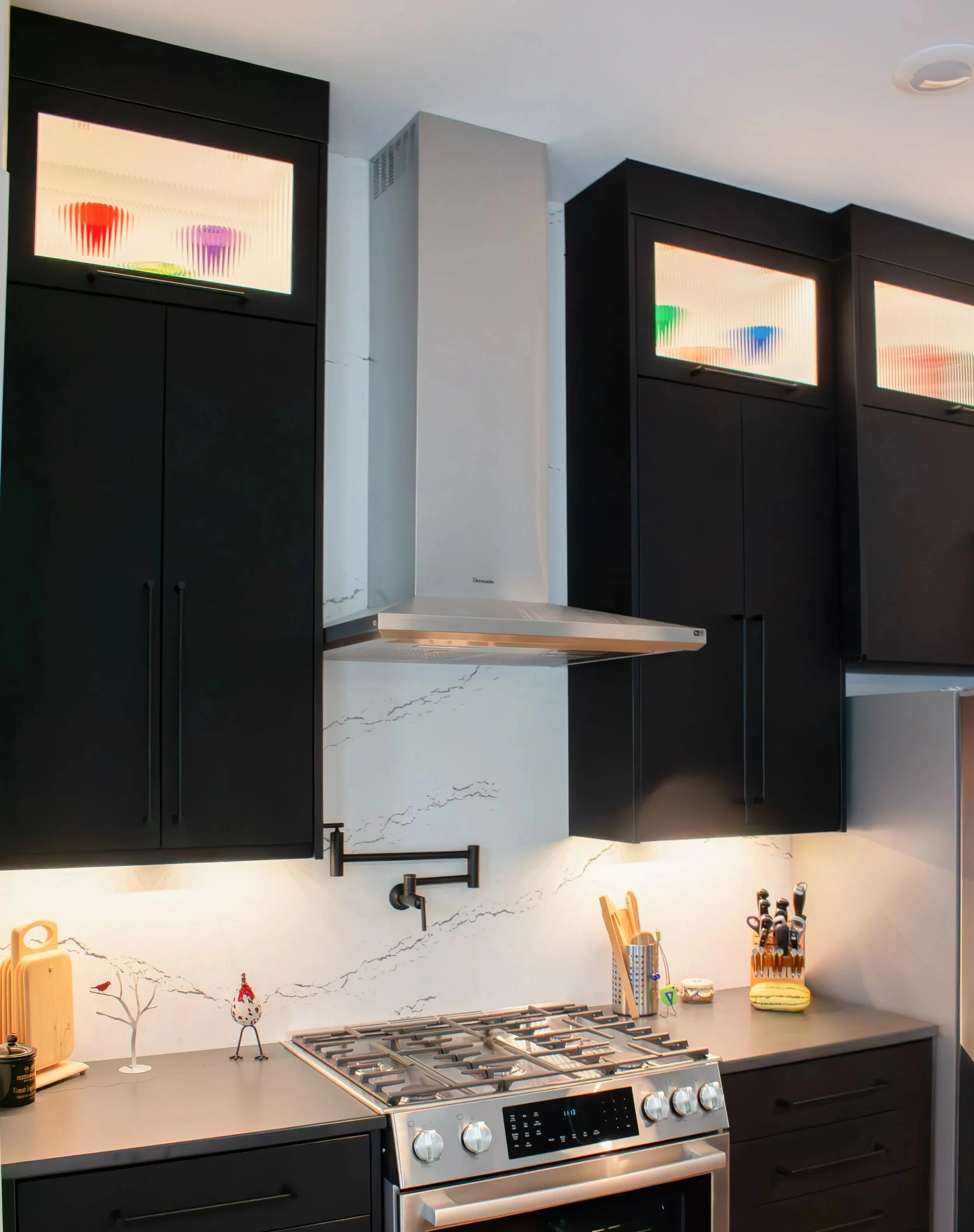 Modern kitchen with black cabinets, a white marble backsplash, a gas stove, a stainless steel range hood, and decorative items on the counter.