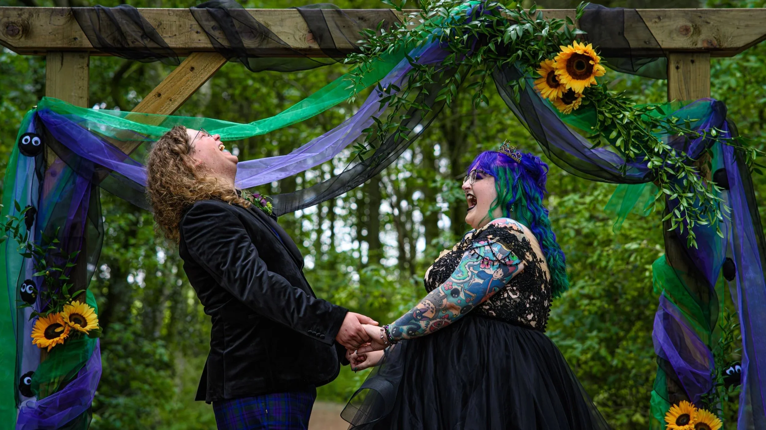 pop punk bride and groom at their wedding ceremony laughing - black wedding dress - bright coloured hair - purple and green wedding decor