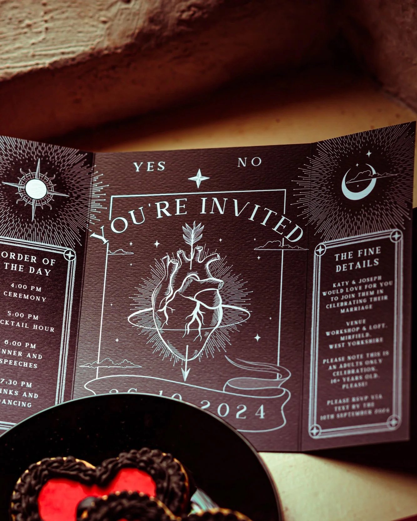 Wedding invitation with celestial and anatomical heart theme, includes event details and RSVP information, presented with white illustrations on dark background.
