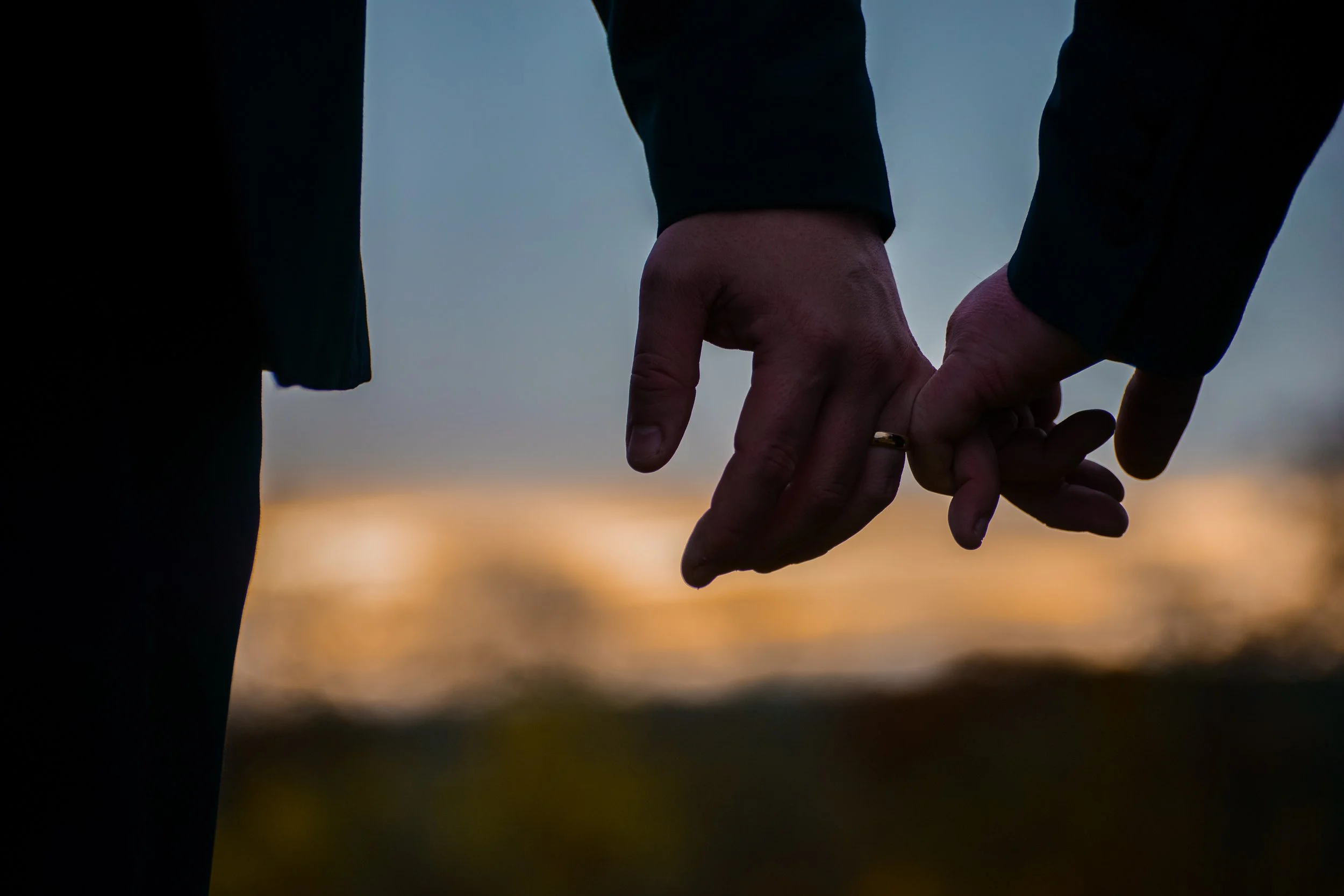 A close-up of two people holding hands outdoors during sunset.