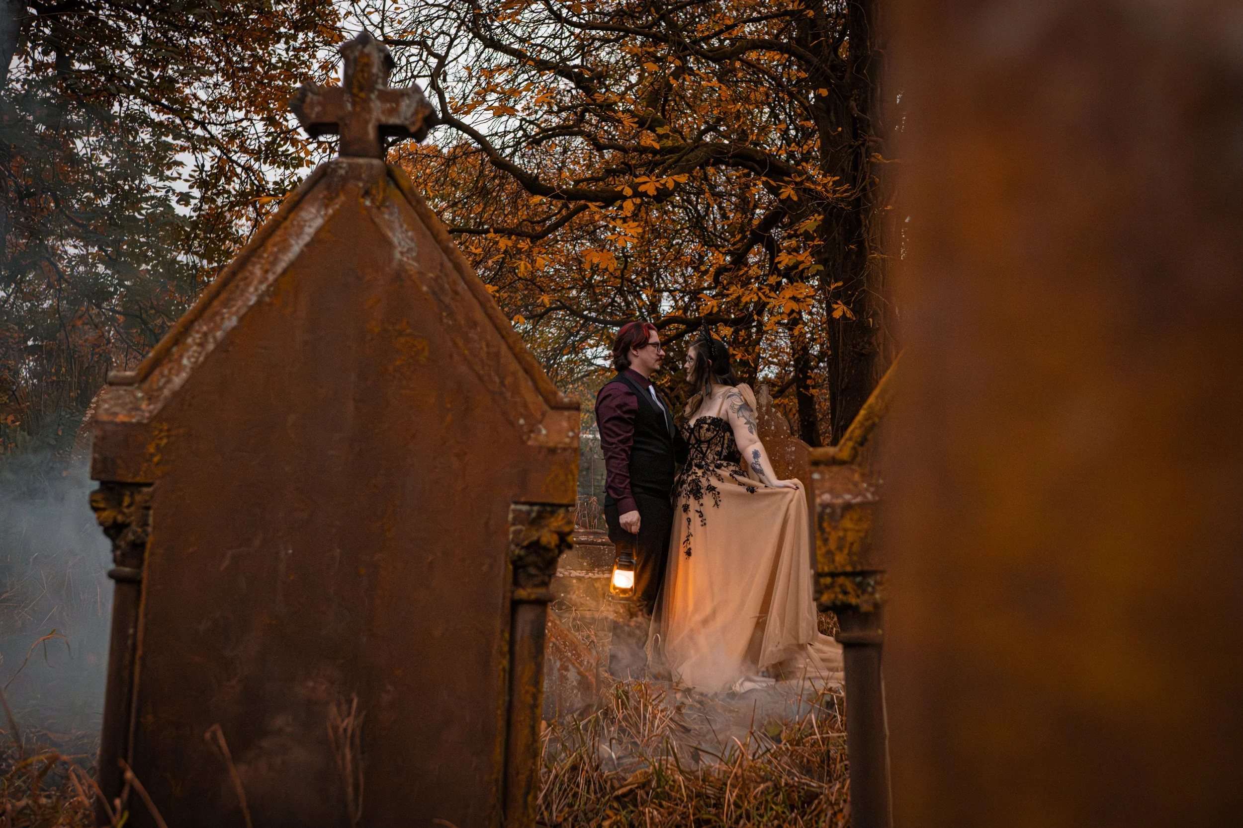 An alternative Husband and Wife standing in an abandoned graveyard, holding a lantern. A post-wedding, first anniversary shoot.