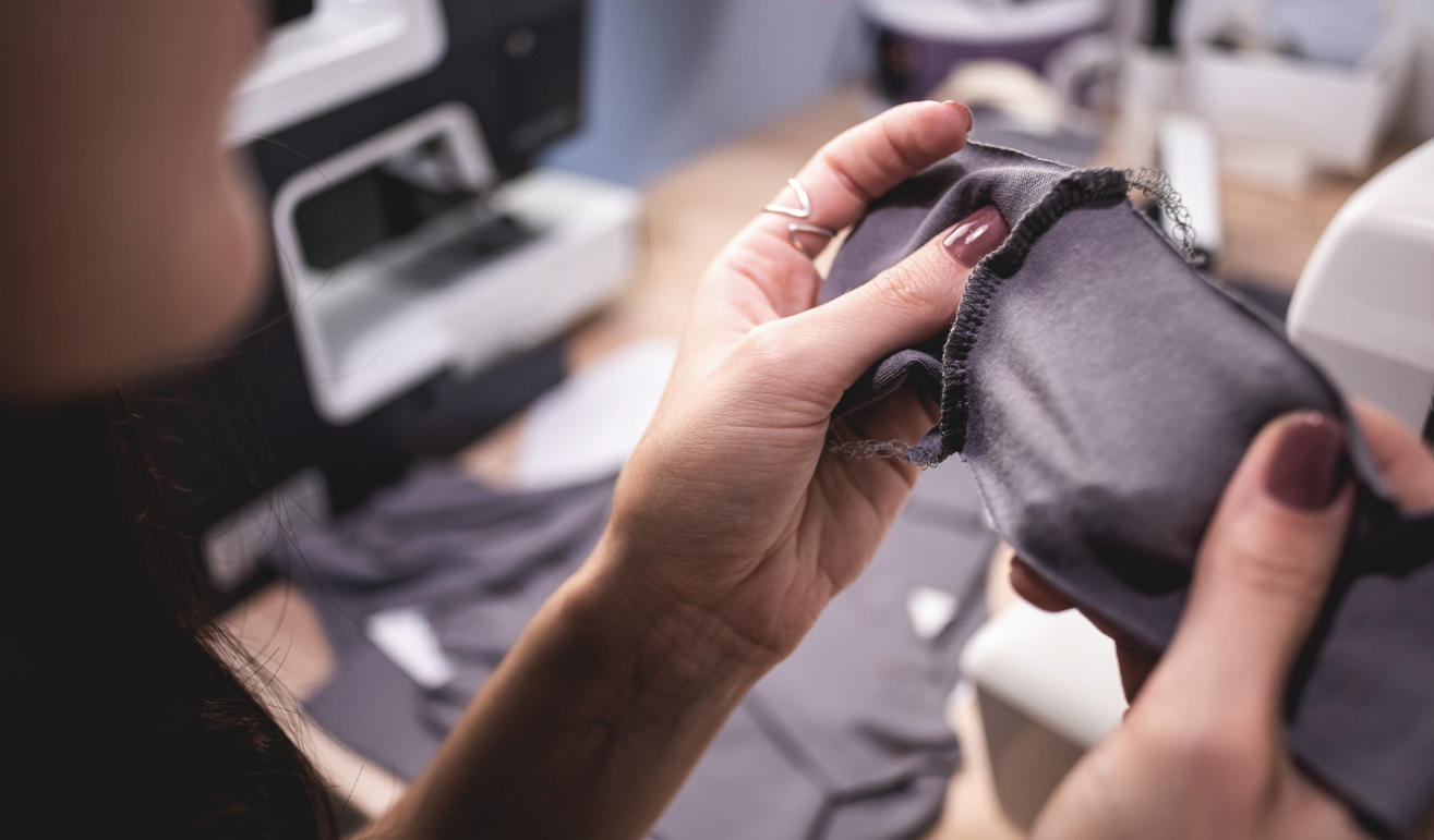 A person sewing or working with gray fabric, possibly on a garment or textile project, in a workshop or studio environment.