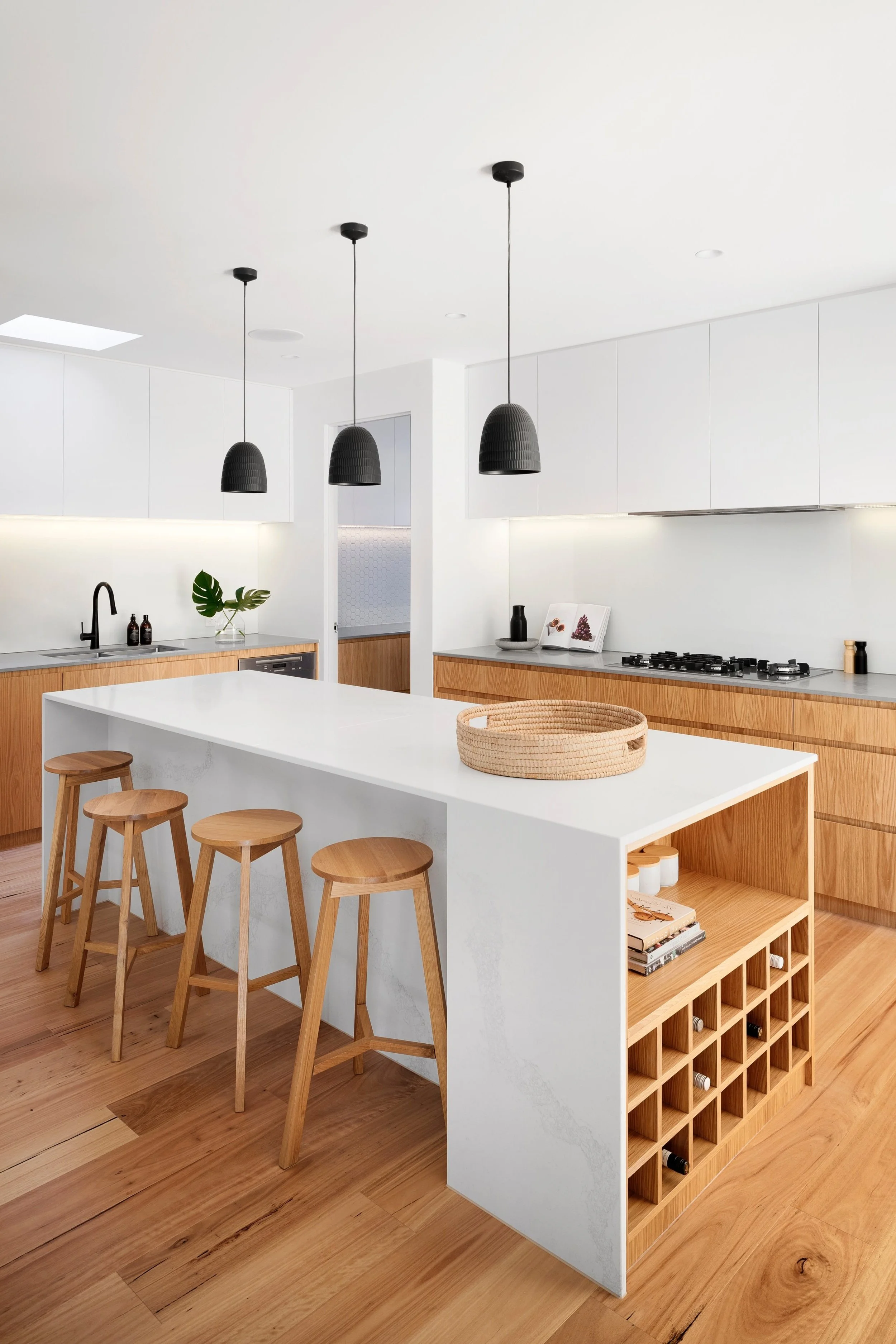 Modern kitchen with white cabinets, a large white island, black pendant lights, and wooden stools and flooring.