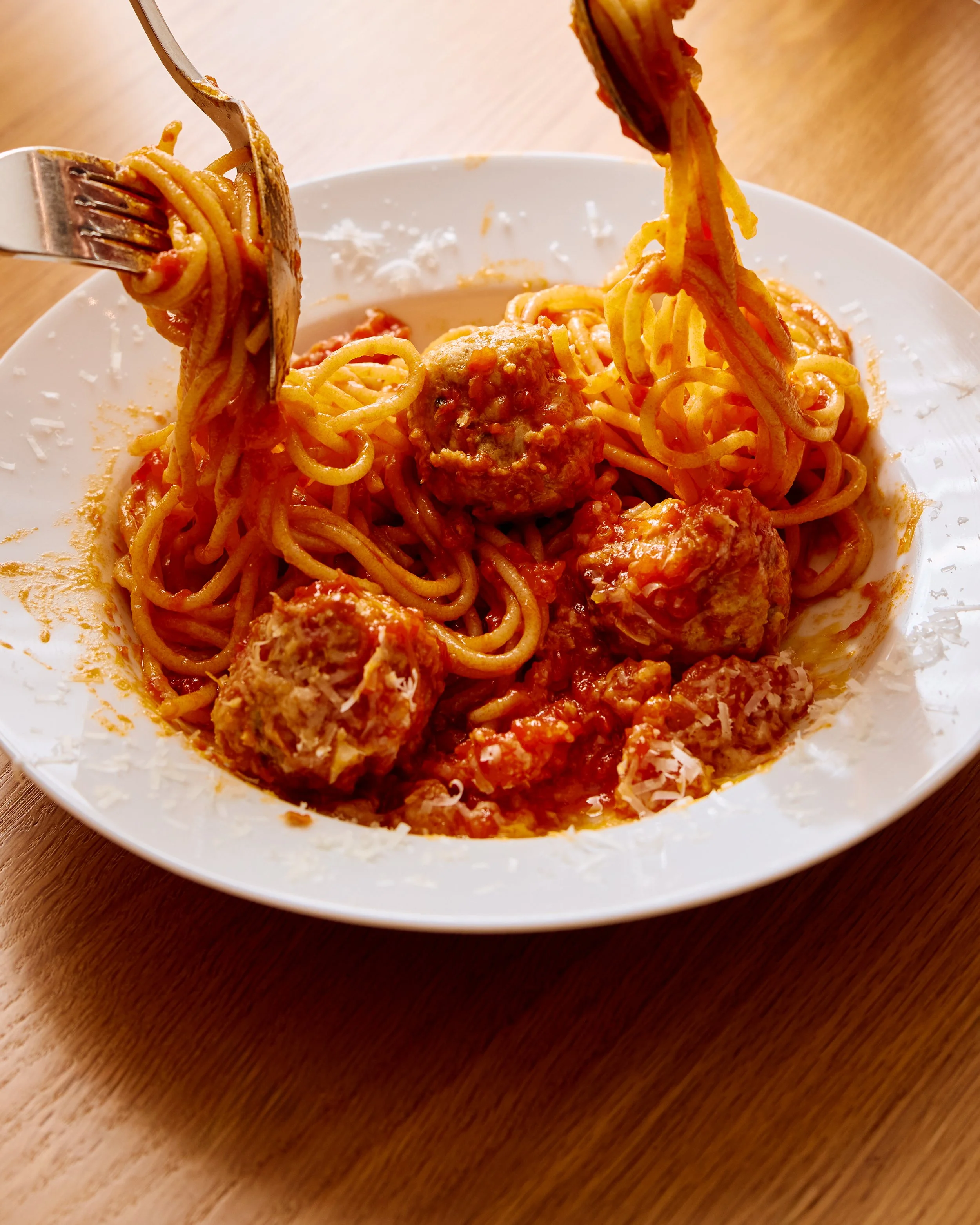 A bowl of spaghetti and meatballs with two forks twirling the pasta