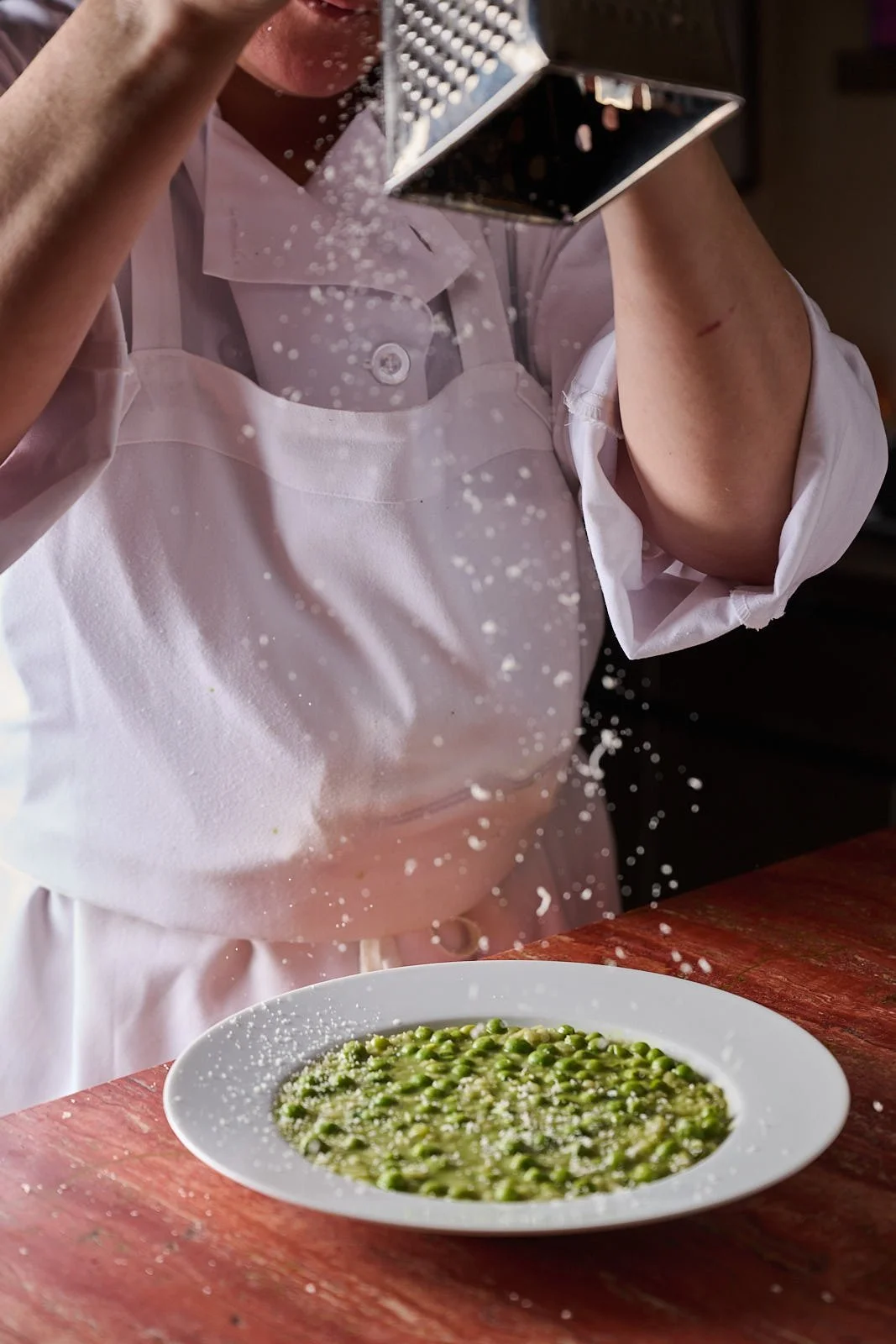 A chef at Jupiter Restaurant grates cheese over a bowl of risi e bisi. 