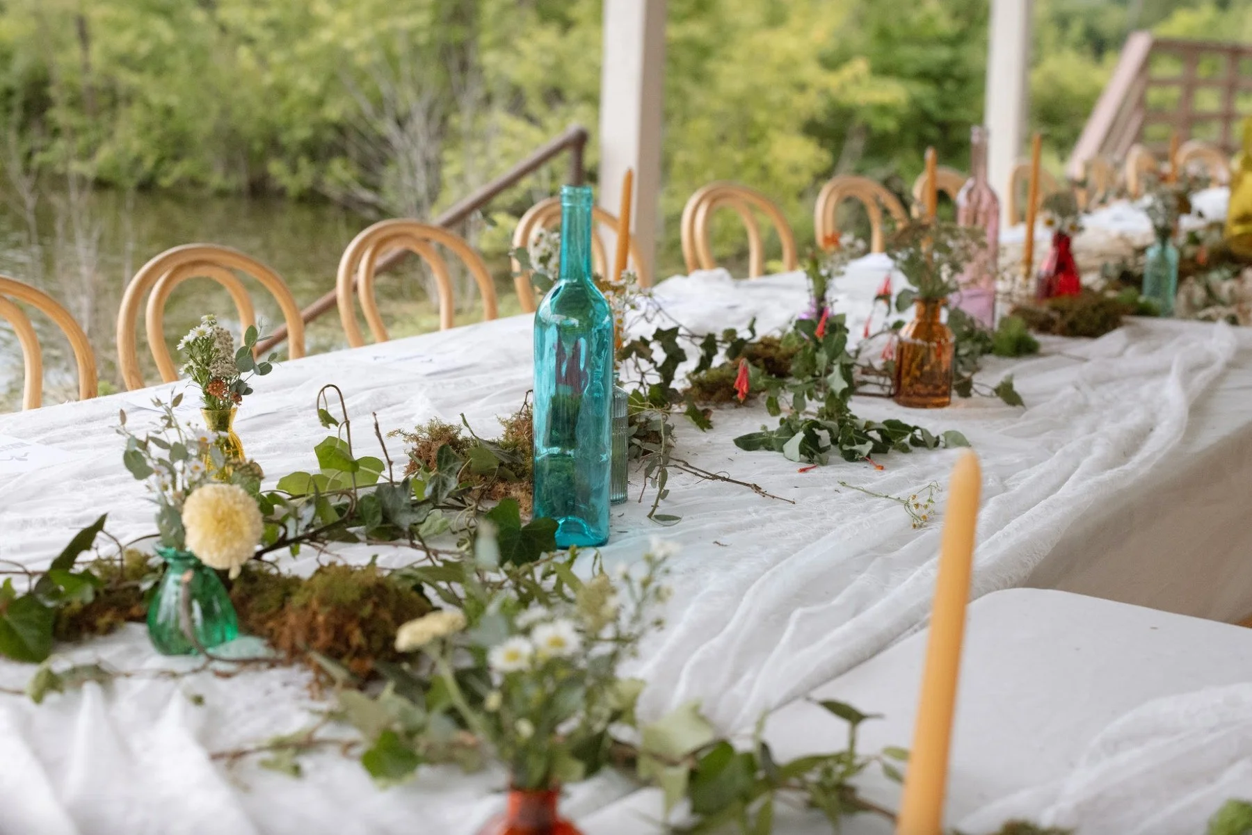 Outdoor wedding reception table with white flowers, candles, and colorful glassware at The Eden Estate.