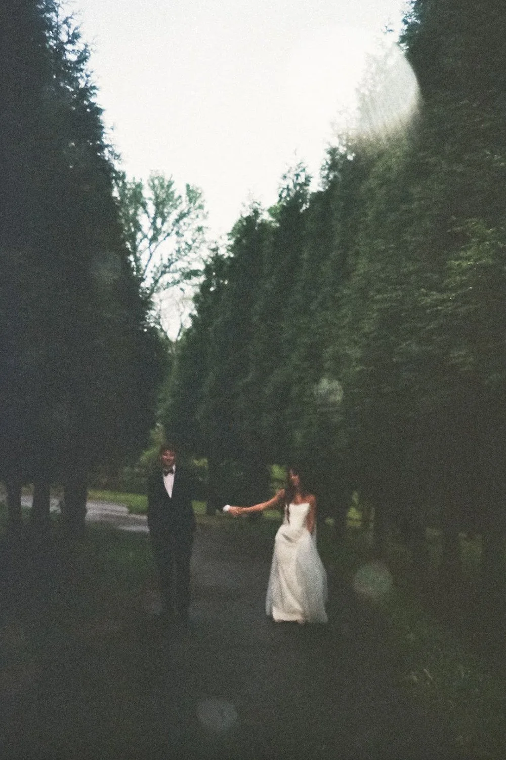 Bride and groom walking along a tree-lined path at The Eden Estate. Photo by Jenna York.