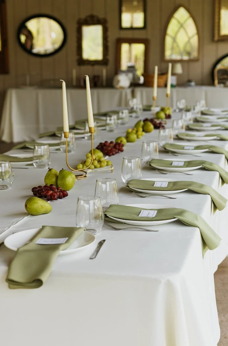 Elegant indoor reception table with white linens, greenery, and place settings.