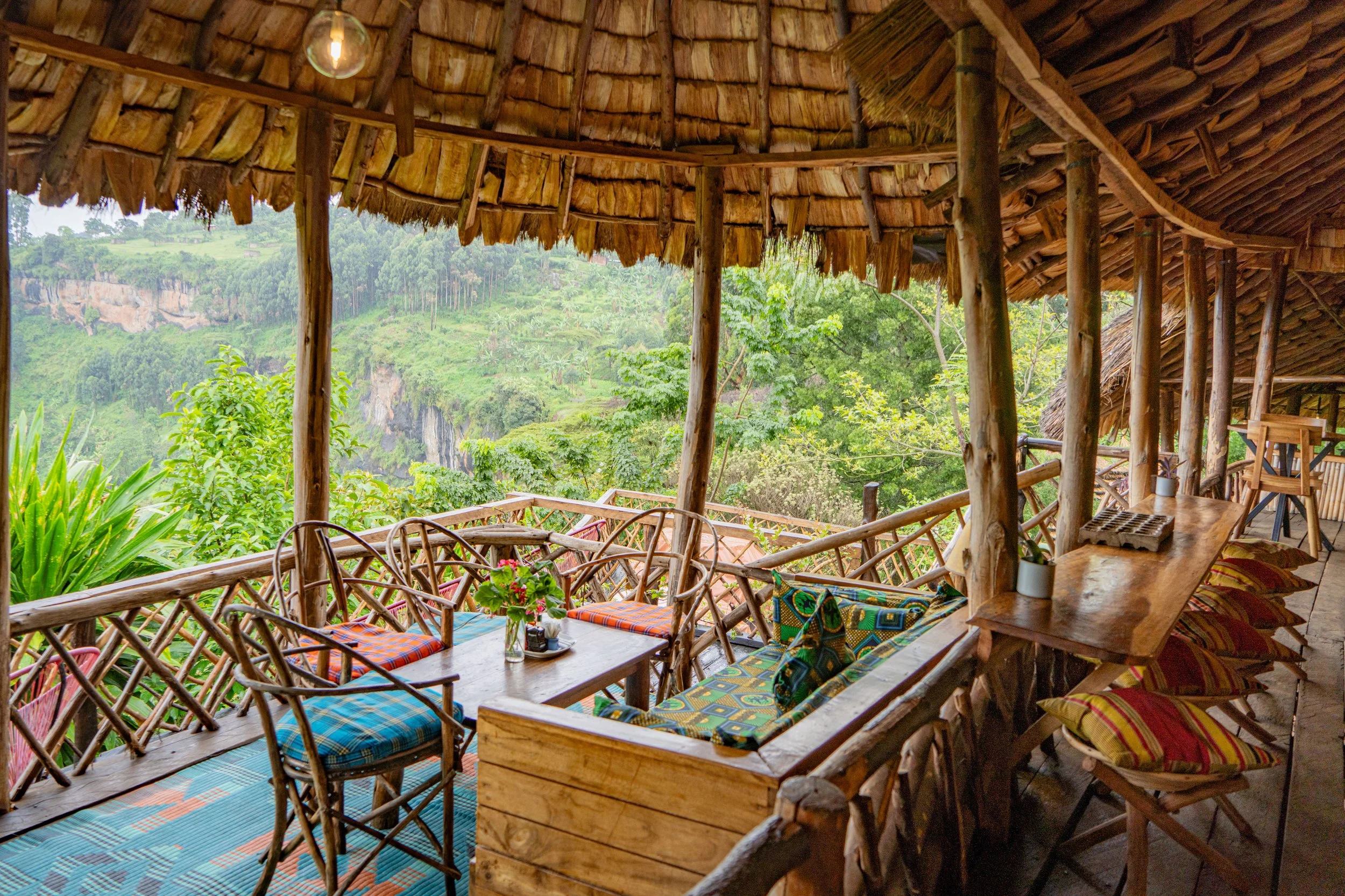Wooden outdoor seating area with colorful cushions, overlooking lush green hillside with trees and cliffs.