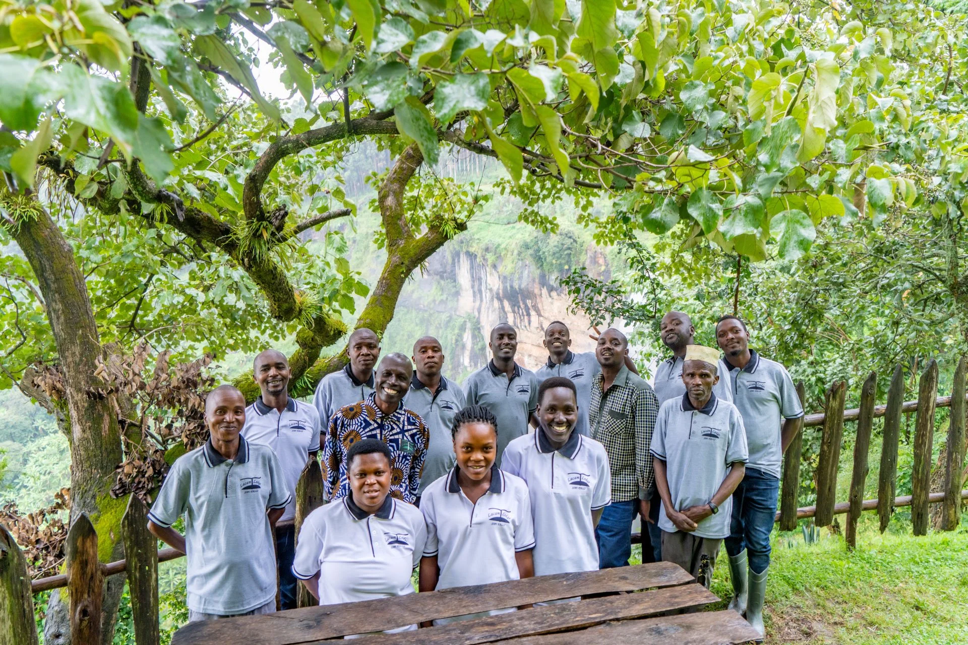 Group of people standing outdoors under a large tree with green leaves, smiling for a photo.
