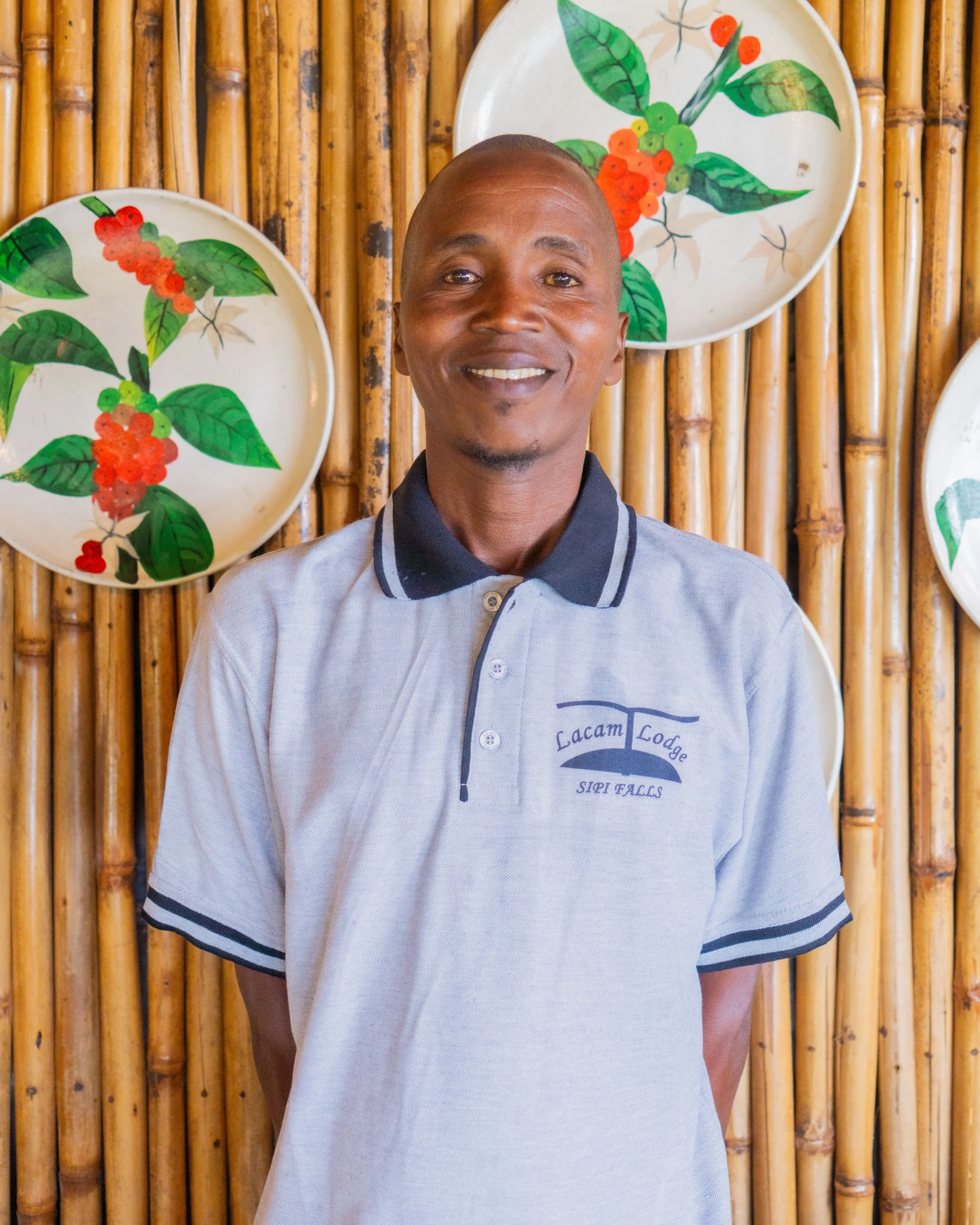 A man standing in front of a bamboo wall with decorative plates featuring coffee plant illustrations.
