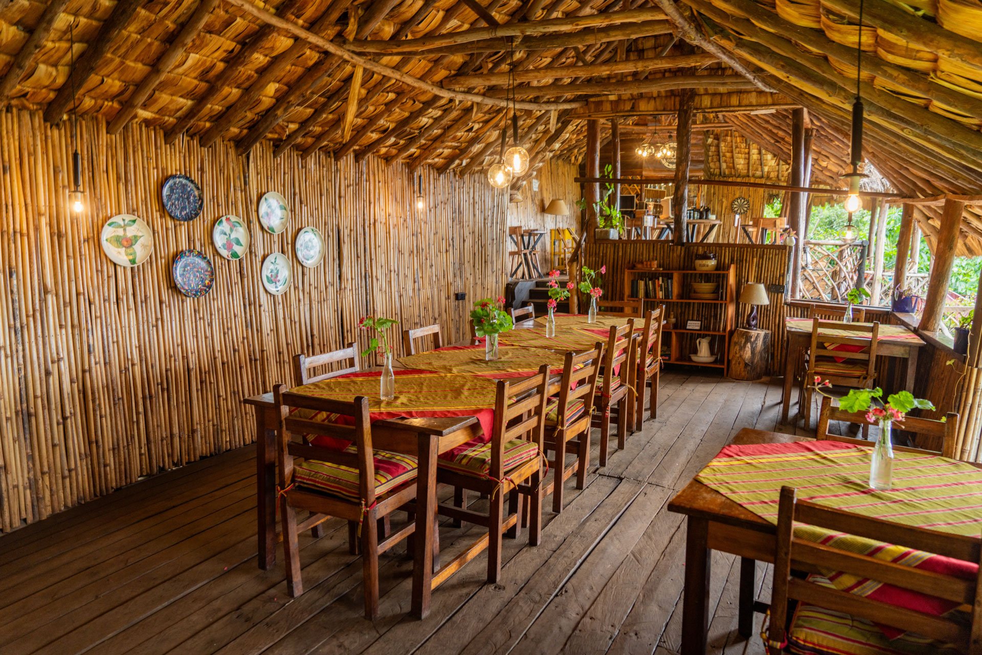 Interior of a rustic restaurant or cafe with wooden walls and ceiling, decorated with hanging light bulbs, and flower vases on tables.