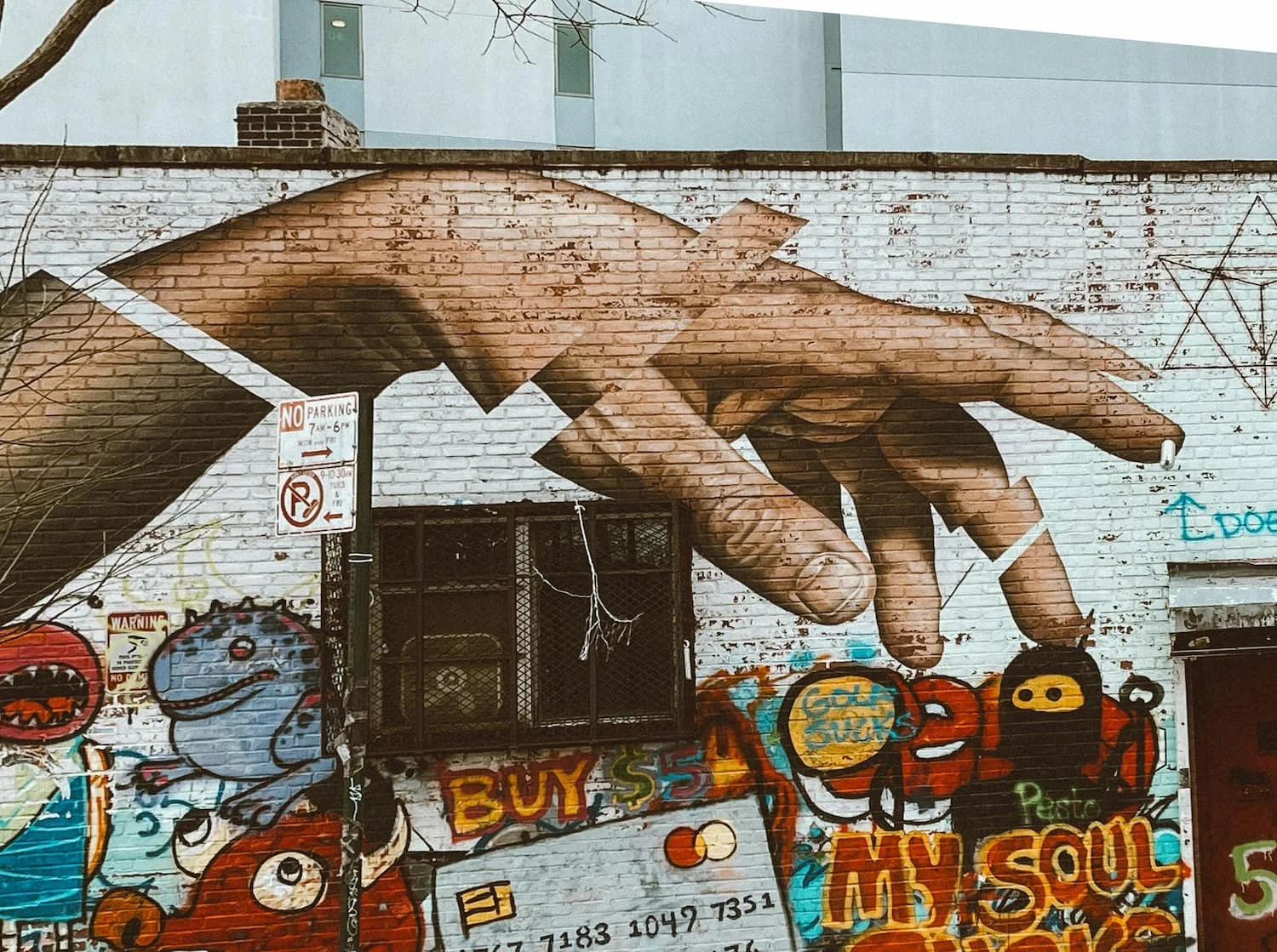 Graffiti on a brick wall depicting a fragmented hand reaching out with the words "buy" and "soul" painted nearby.Reaching for what matters, we reconnect with the parts of ourselves that endure.
