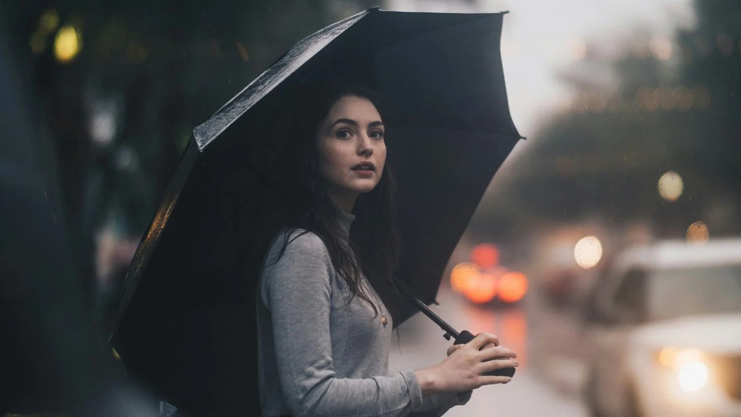 Woman holding an umbrella in rainy weather, looking hopeful and thoughtful, symbolizing resilience and finding calm during challenging times.