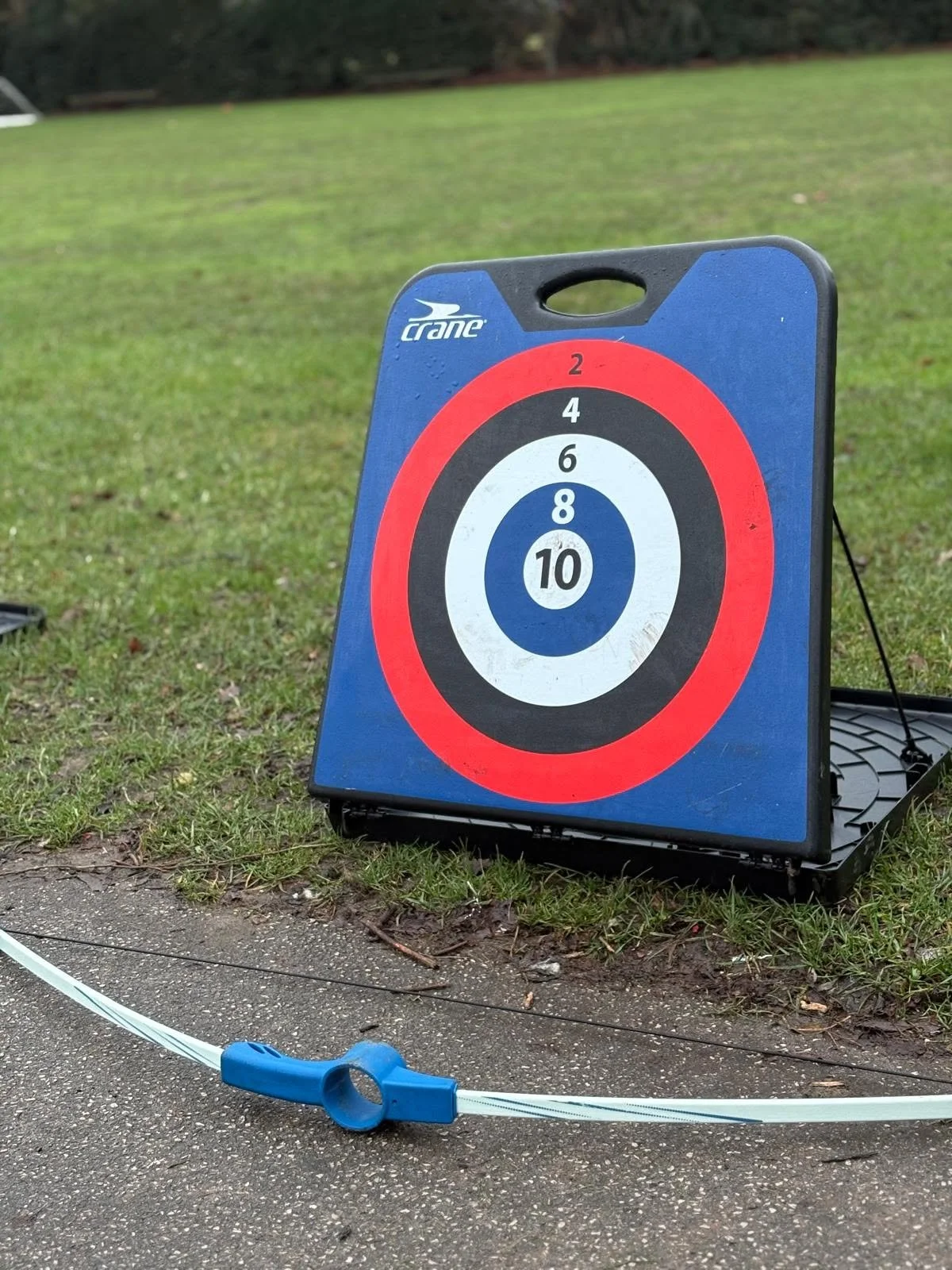 A target board used for archery training, placed outdoors on the grass, with concentric circles in white, black, and red, numbered for scoring.