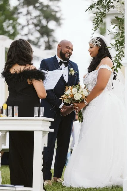 The bride and groom stand before Rev. Benita gazing at each other with excitement while Rev. Benita officiates their wedding helpd at the Neuse Breeze Wedding Venue in  Havelock, NC.