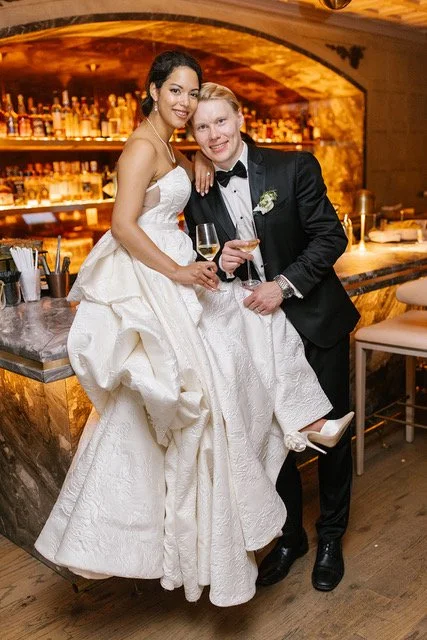 The bride sits atop of the bar beside her groom holding glasses of champaign during their reception at The Hermitage Hotel.