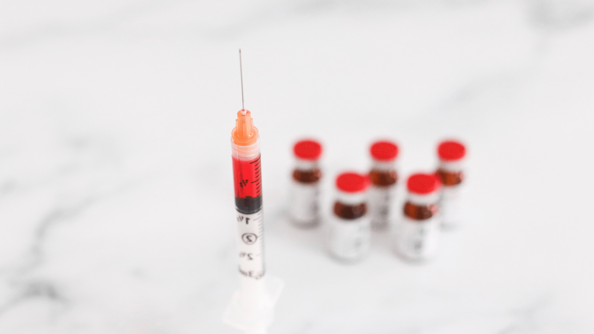 A syringe filled with blood and six small vials with red caps