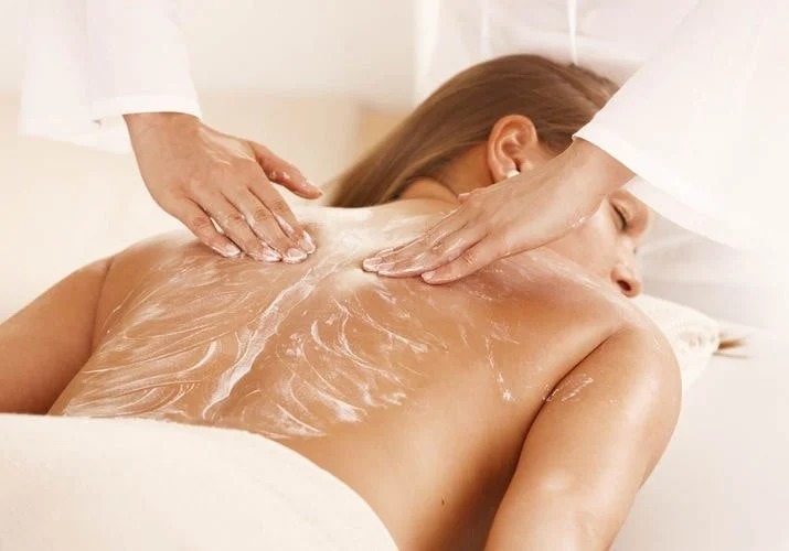A woman receives a massage on her back at a spa, with a massage therapist applying oil or lotion.